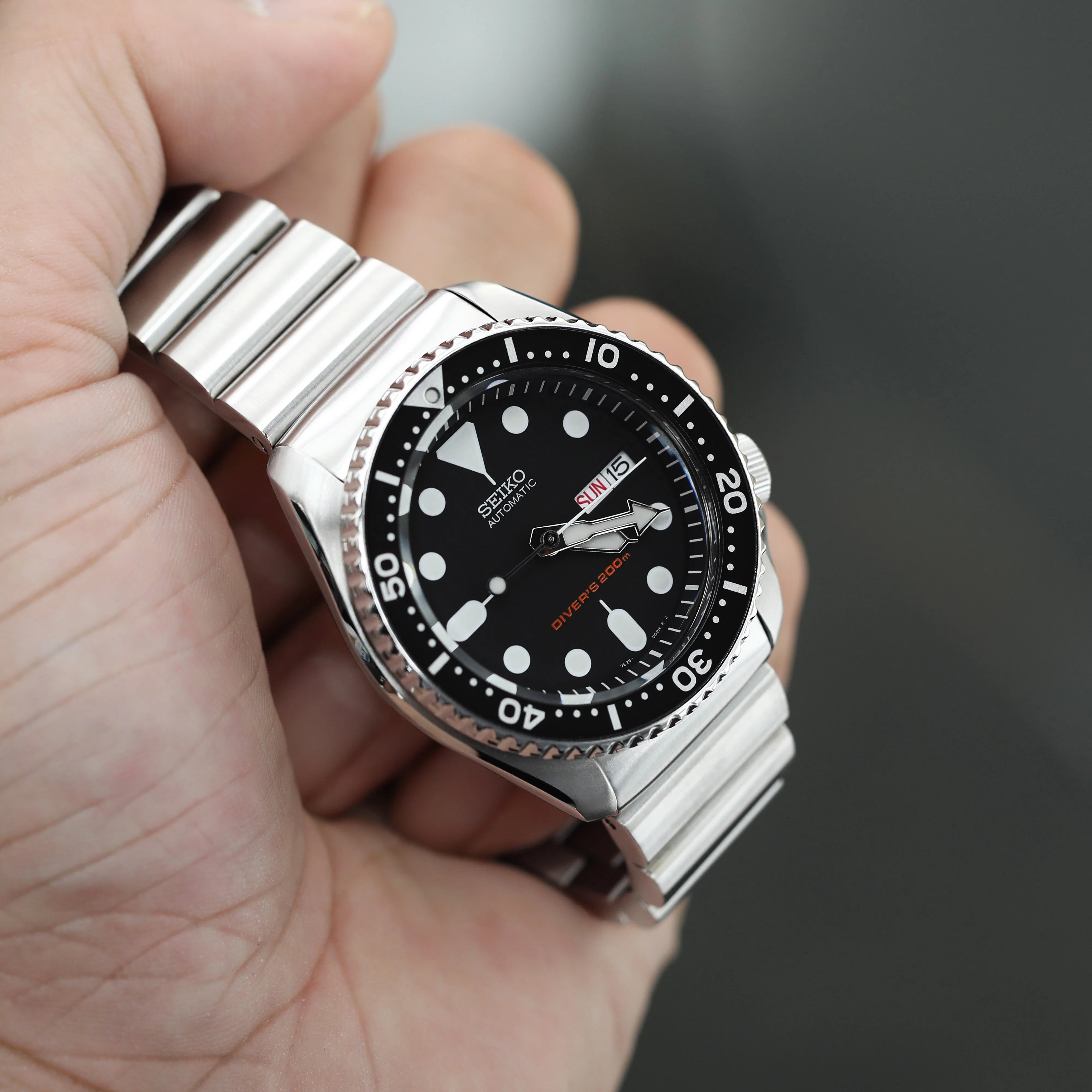 Seiko SKX007 dive watch with stainless steel Bandoleer bracelet held in hand, featuring black dial and rotating bezel