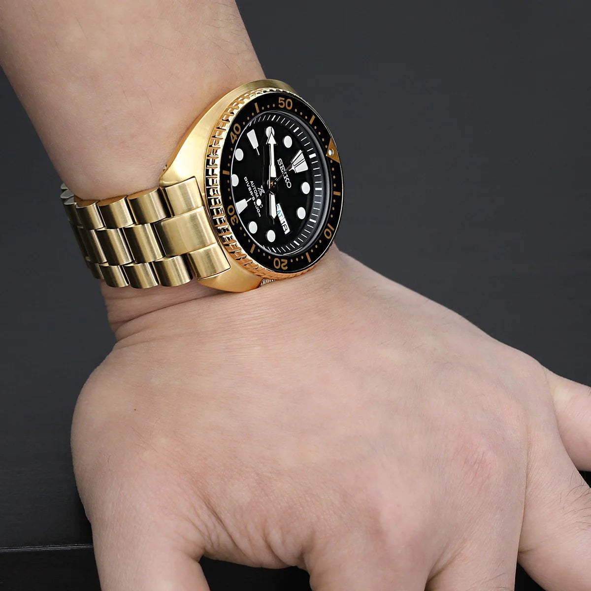 Gold dive watch with black dial and rotating bezel worn on wrist with matching gold metal bracelet