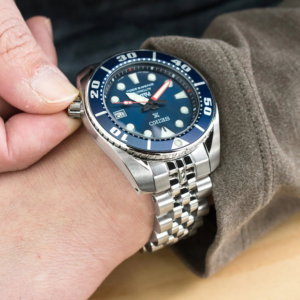 Strapcode Angus-J Louis stainless steel bracelet on Seiko Sumo dive watch with blue dial, worn on wrist with gray fabric sleeve