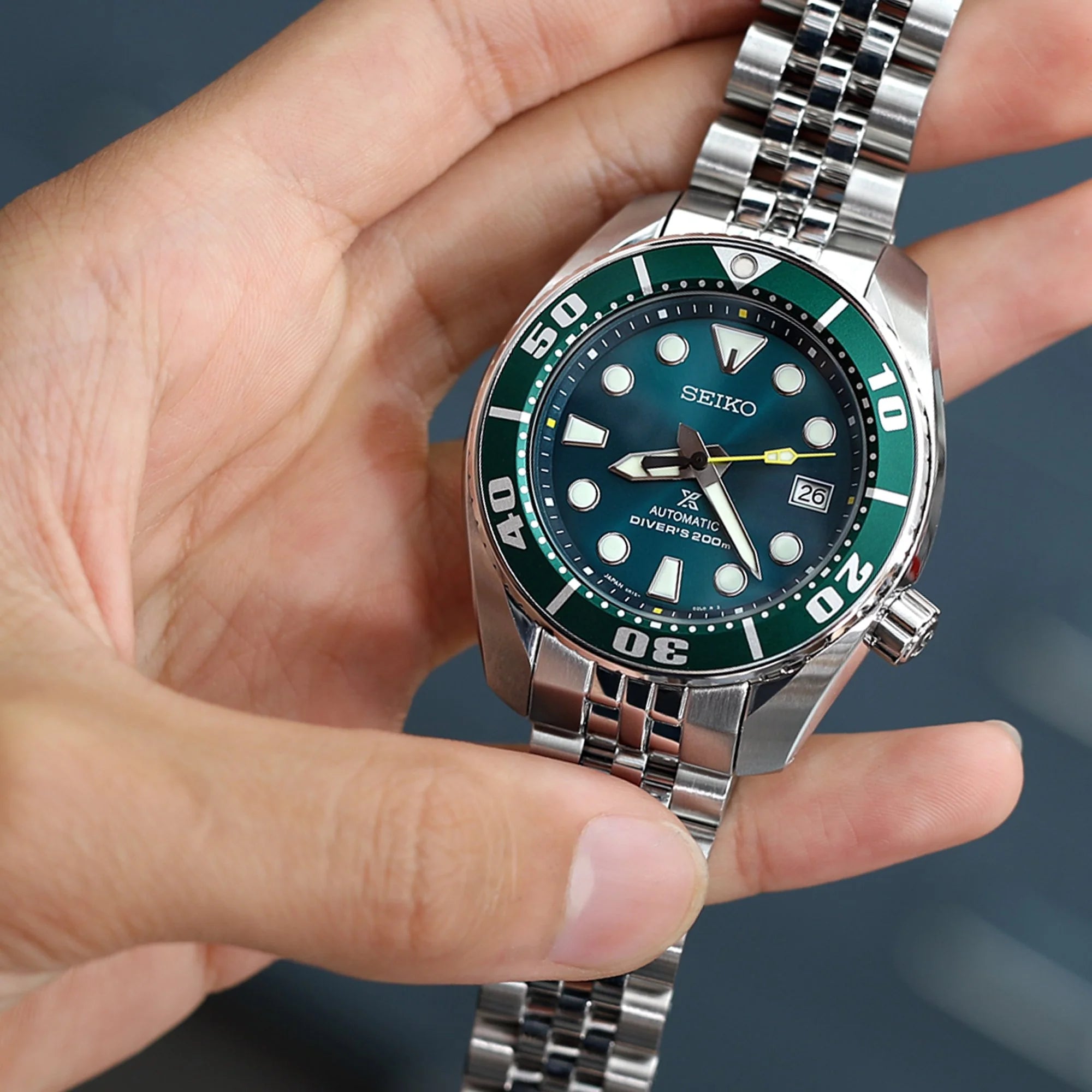 Seiko automatic diver's watch with green dial and stainless steel bracelet held in hand