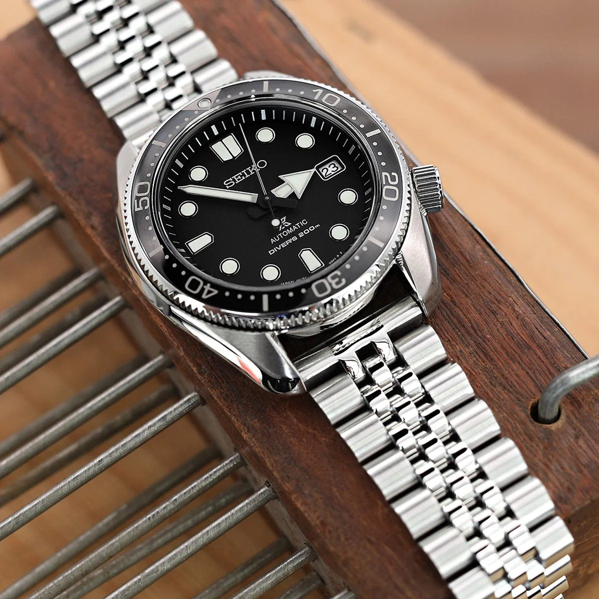Seiko diver watch with stainless steel jubilee bracelet and black dial on wooden surface