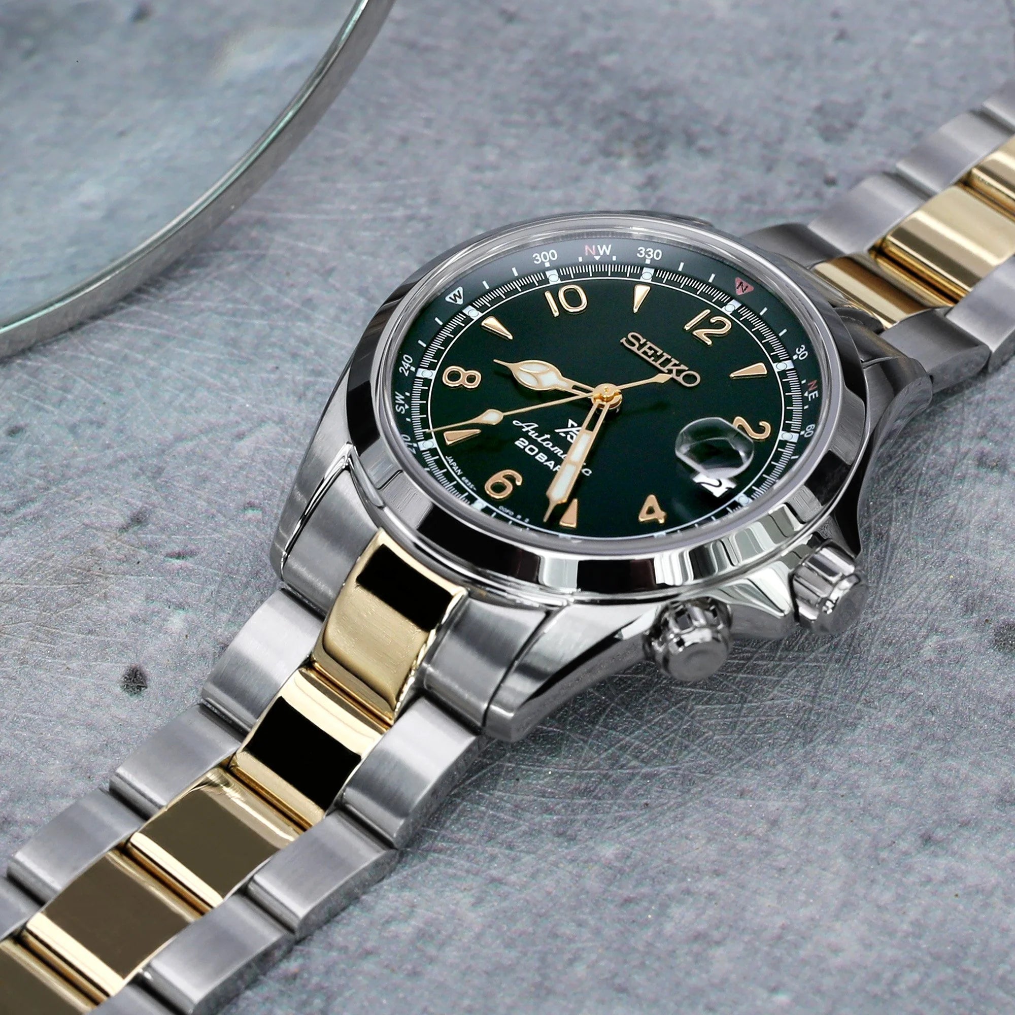 Seiko Alpinist SARB017 watch with two-tone silver and gold bracelet on gray textured surface