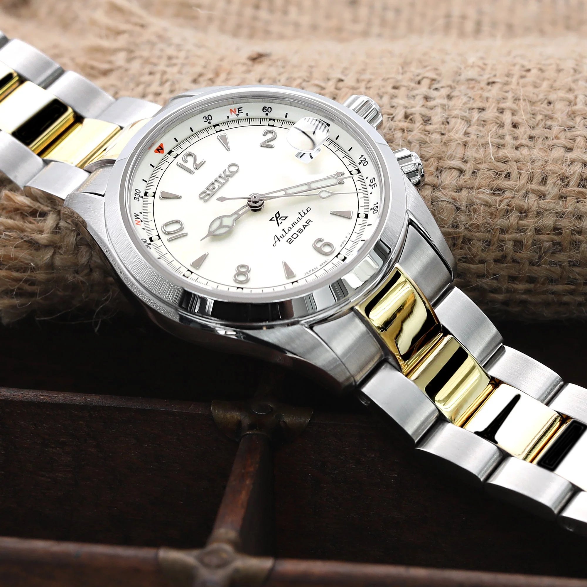 Seiko Alpinist SARB017 two-tone watch with silver and gold bracelet on rustic wooden background