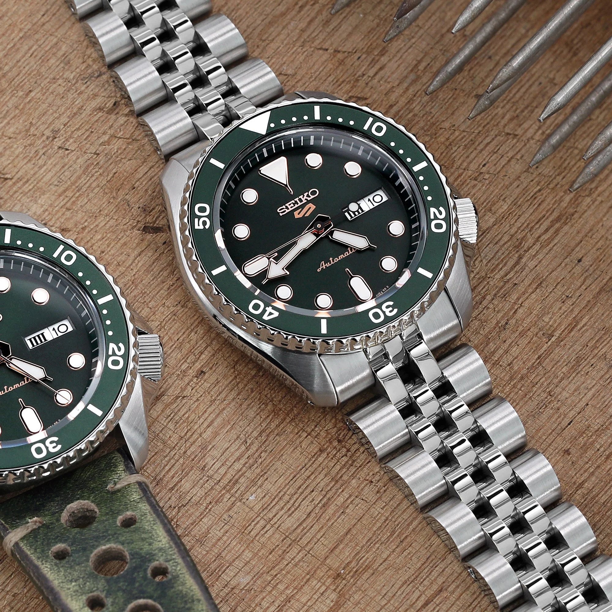 Stainless steel Angus-J Louis bracelet fitted on Seiko 5 watch with green dial and bezel, displayed on wooden surface