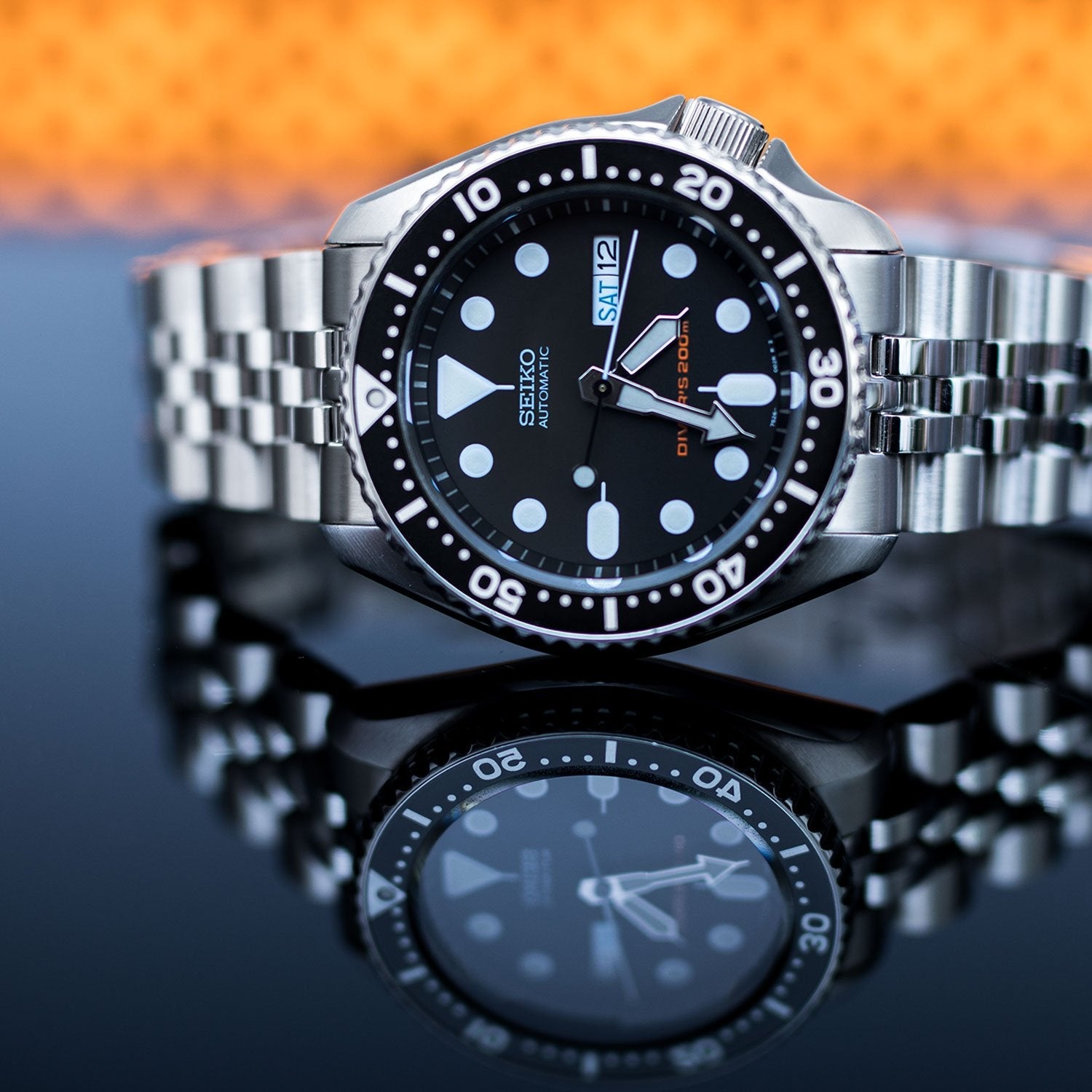 Seiko SKX007 automatic dive watch with stainless steel jubilee bracelet and black dial against sunset background