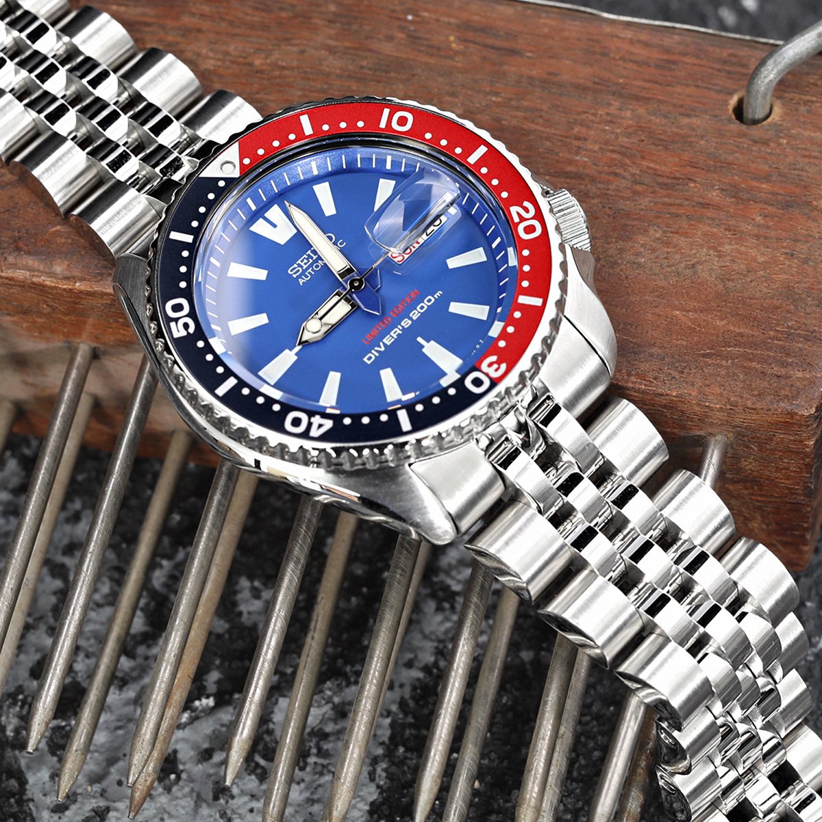 Seiko SKX007 dive watch with blue dial, red and black bezel, stainless steel Angus-J Louis Jubilee bracelet on wooden surface