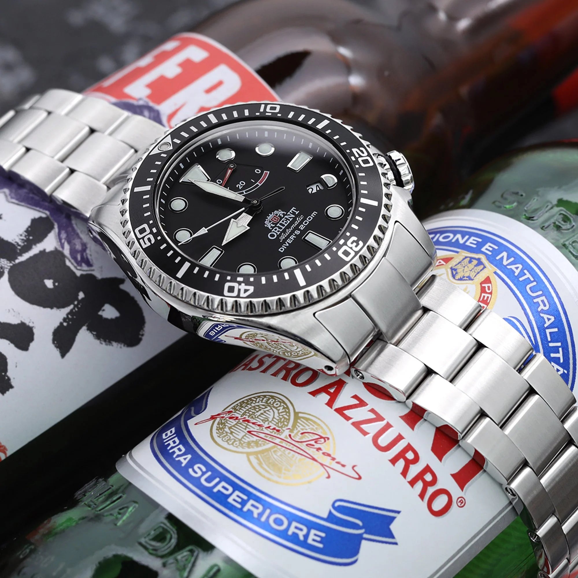 Stainless steel diver watch with black dial on metal bracelet, displayed with beer cans