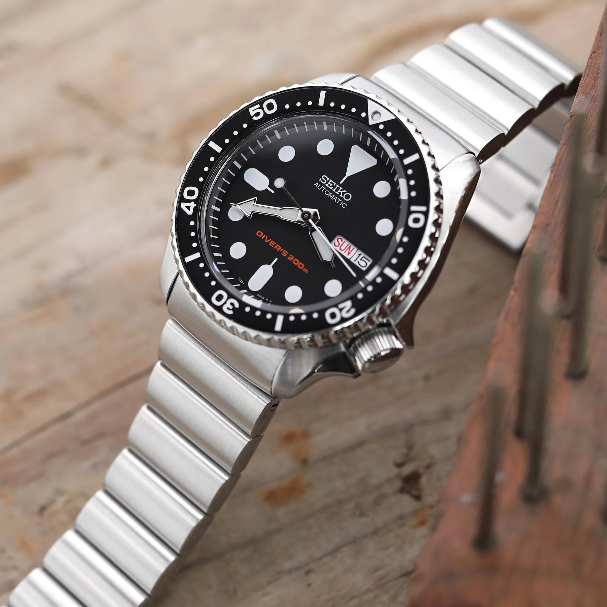 Seiko SKX007 automatic diver watch with black dial, white markers, steel bracelet and rotating bezel on wooden surface
