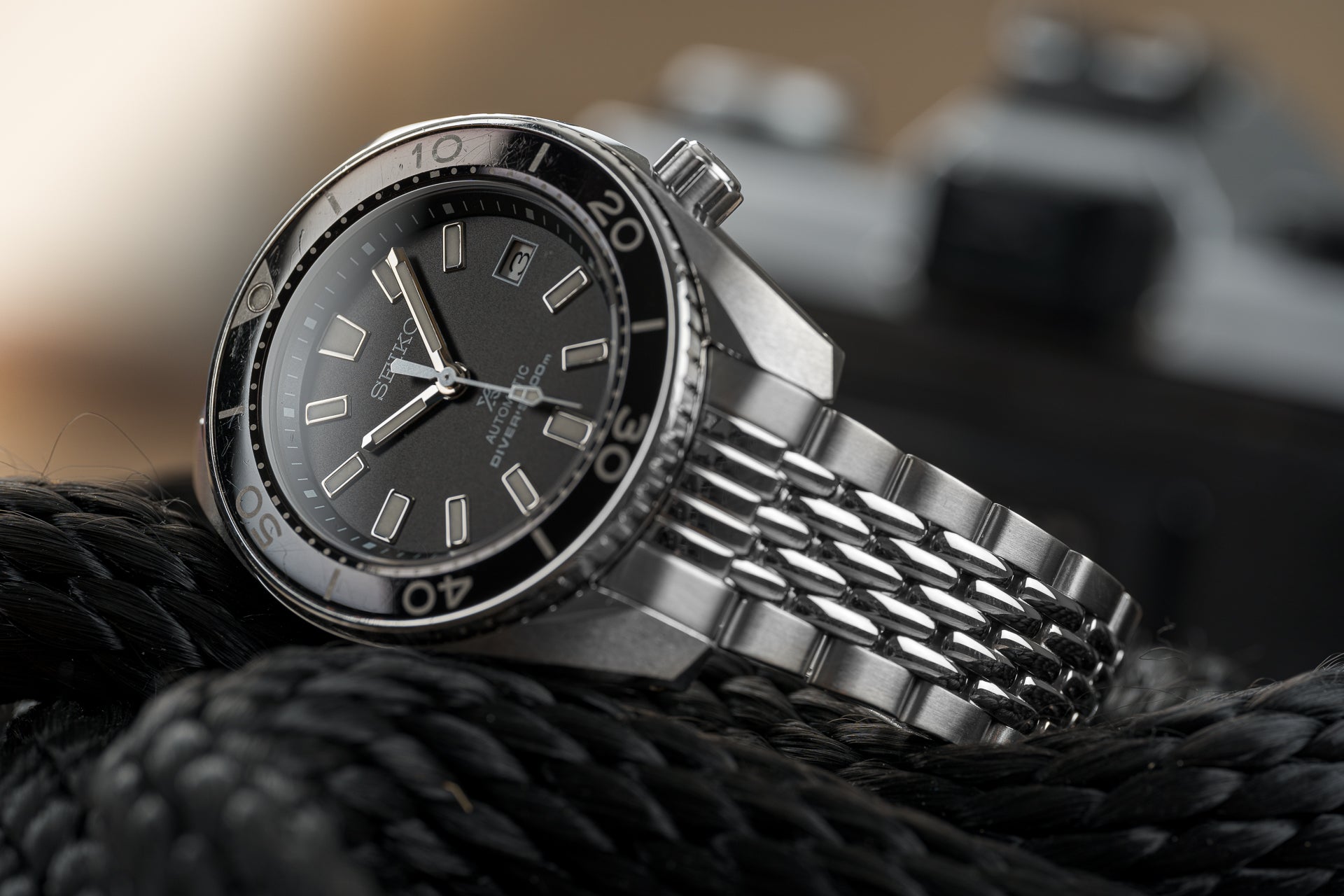 Seiko Sumo stainless steel dive watch with black dial and beads of rice metal bracelet on rope background