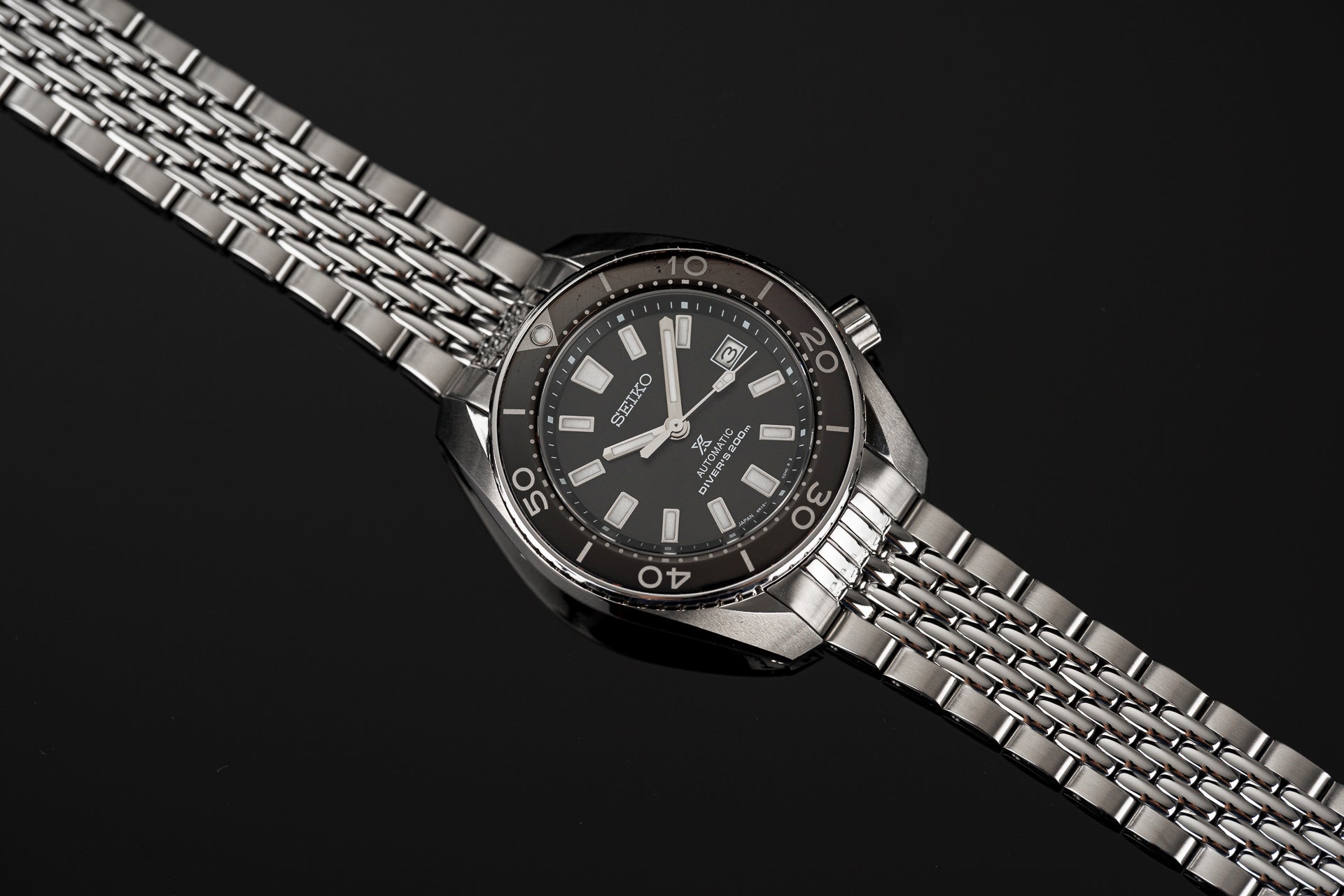 Seiko Sumo stainless steel automatic diving watch with black dial, date window, and beads of rice metal bracelet on dark background