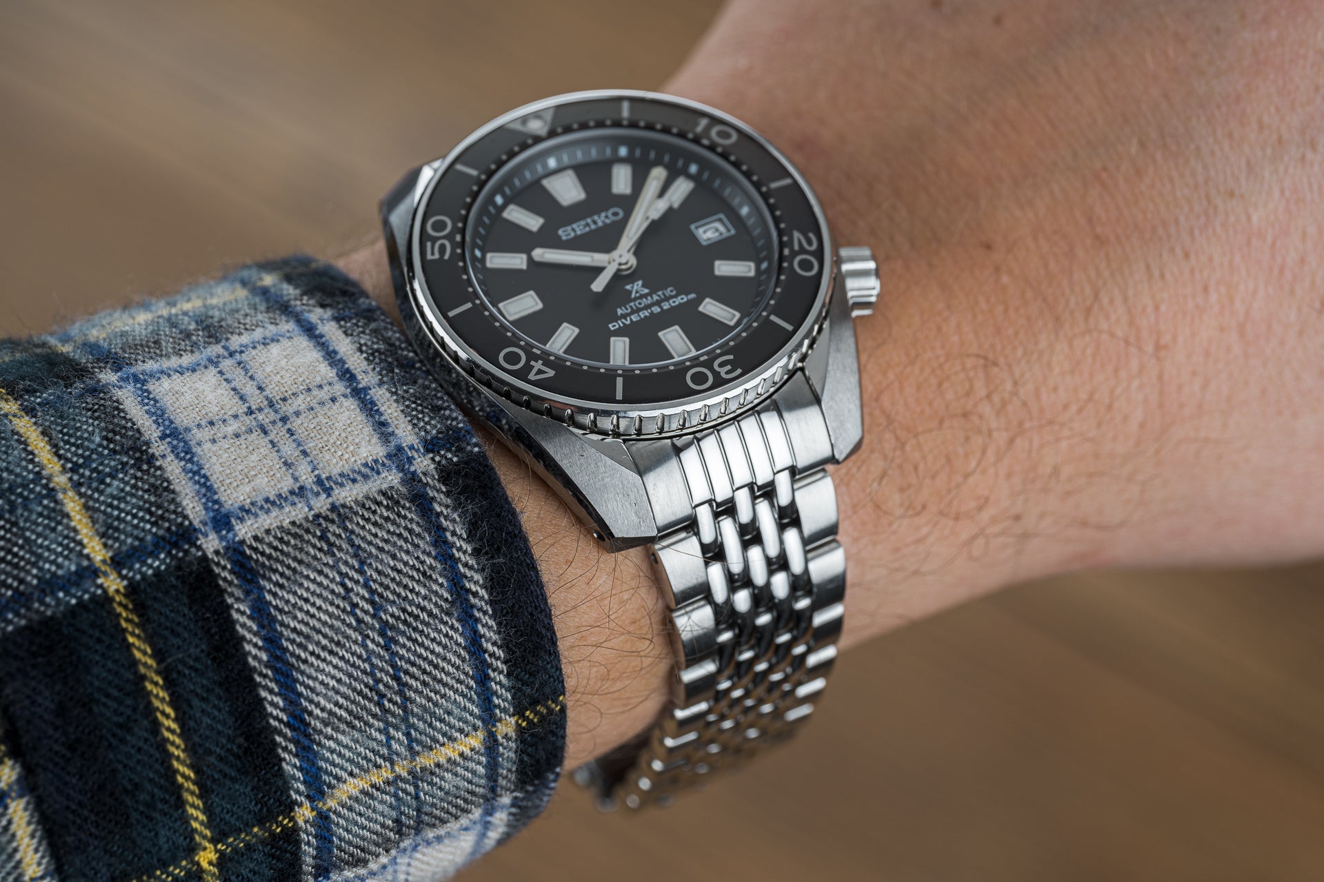Seiko Sumo automatic dive watch with black dial, stainless steel beads of rice bracelet, worn on wrist with plaid shirt