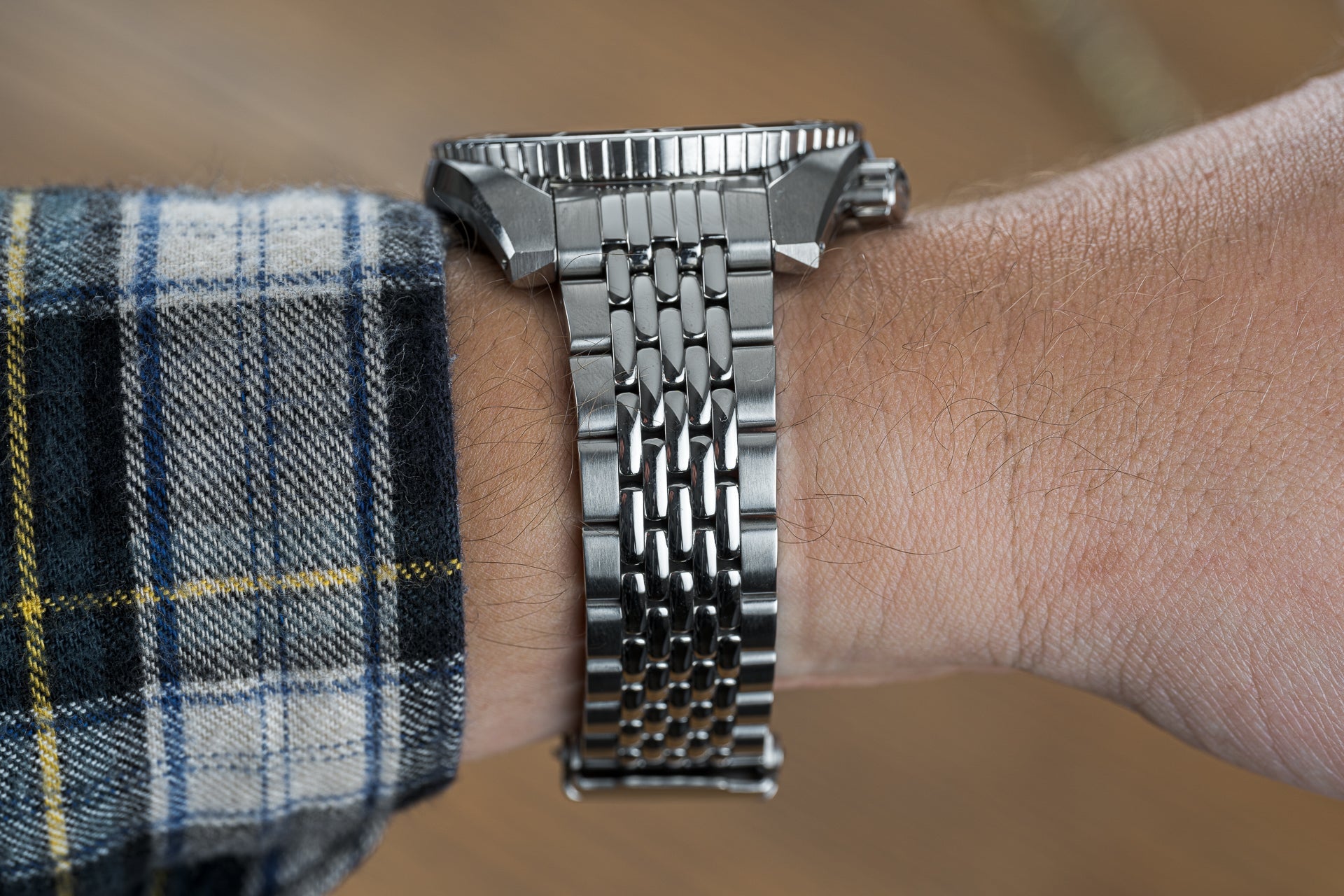 Stainless steel beads of rice watch bracelet on wrist with plaid shirt cuff, showing detailed link construction and polished finish