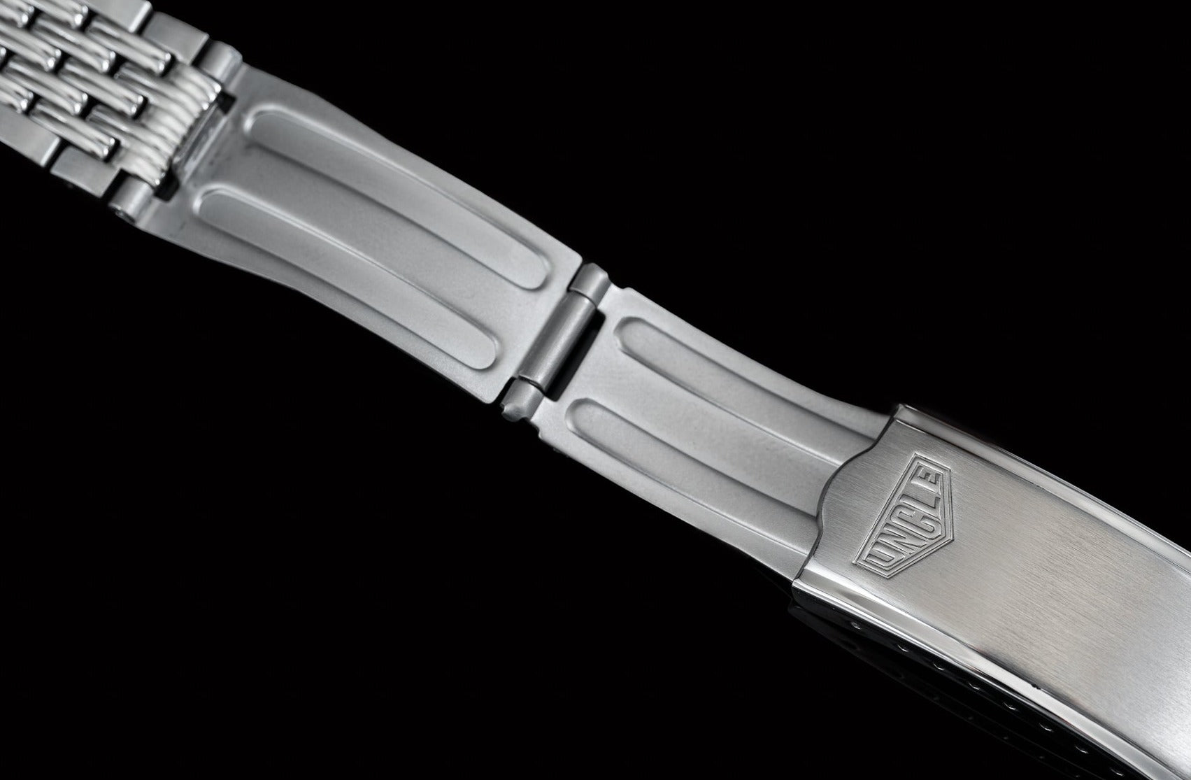 Polished stainless steel bracelet with beads of rice links and Tag Heuer Carrera clasp on black background