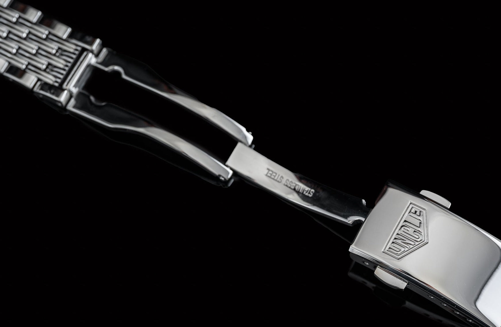 Stainless steel beads of rice bracelet with polished Tag Heuer Carrera logo buckle against black background