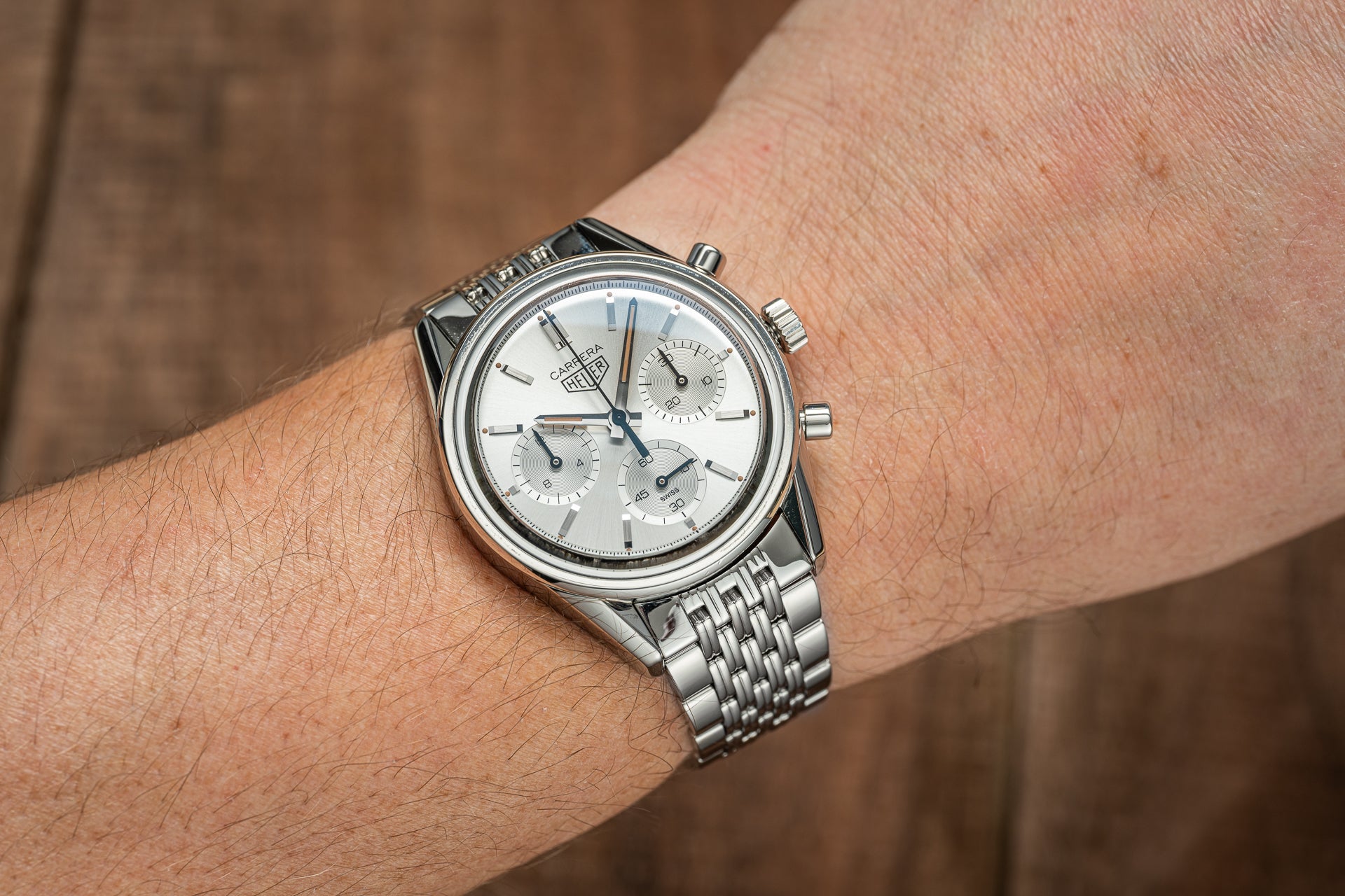 Stainless steel chronograph watch with white dial and subdials worn on wrist with beads of rice metal bracelet