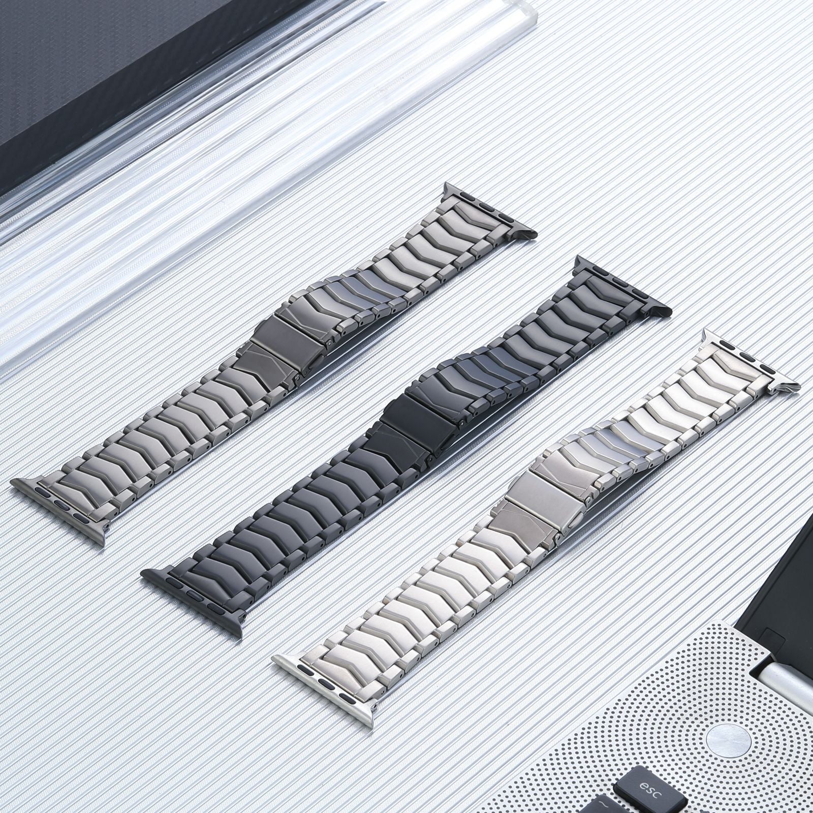 Titanium arched bracelet bands for Apple Watch in silver, space black and graphite finishes displayed side by side