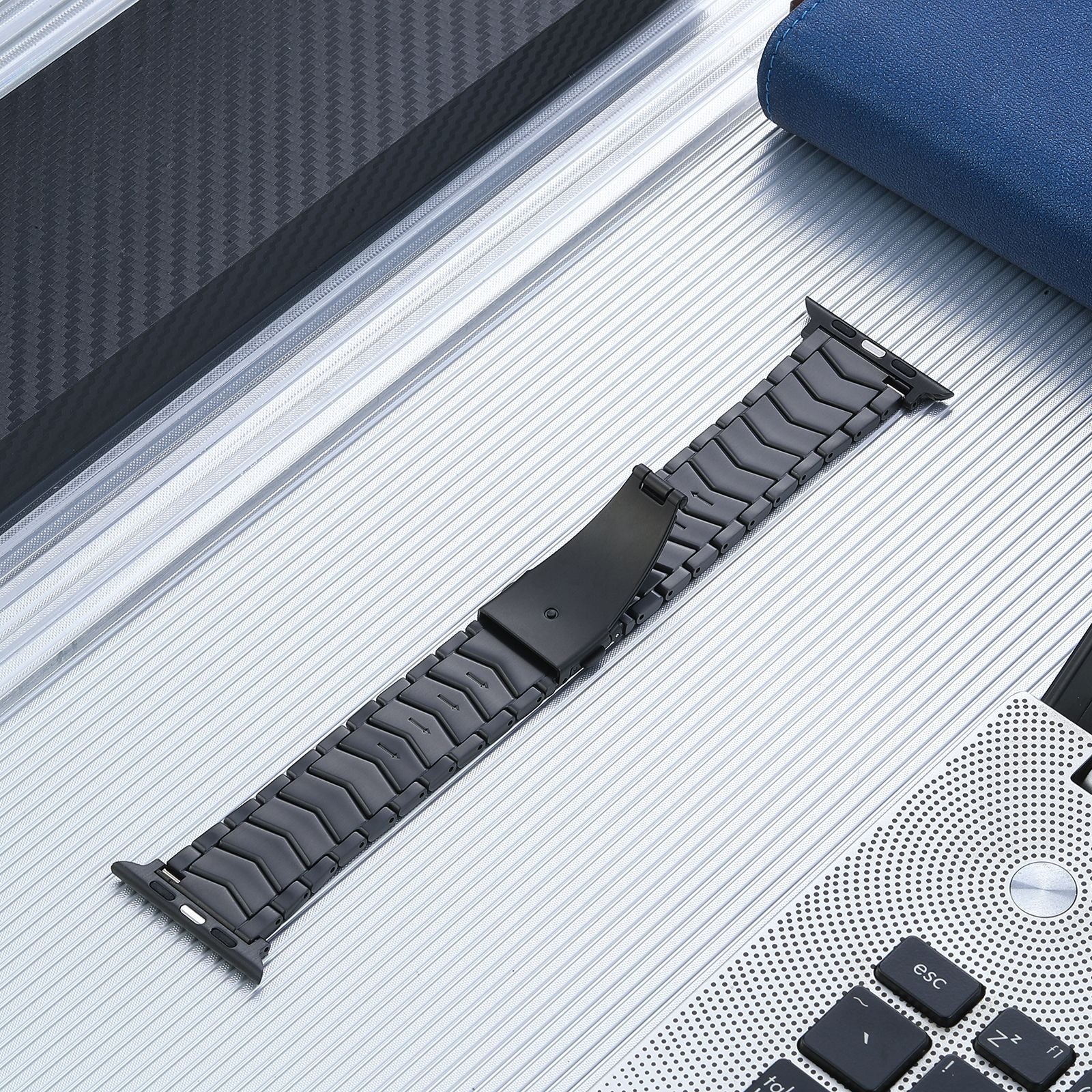 Black titanium link bracelet for Apple Watch with curved design and connector attachment on silver aluminum surface
