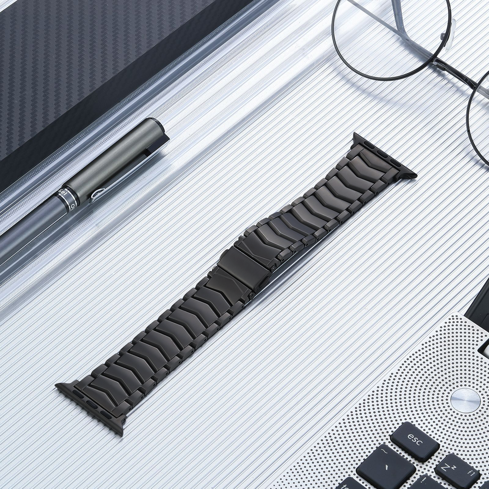 Black titanium link bracelet for Apple Watch with curved design and connector, displayed with smartwatch accessories