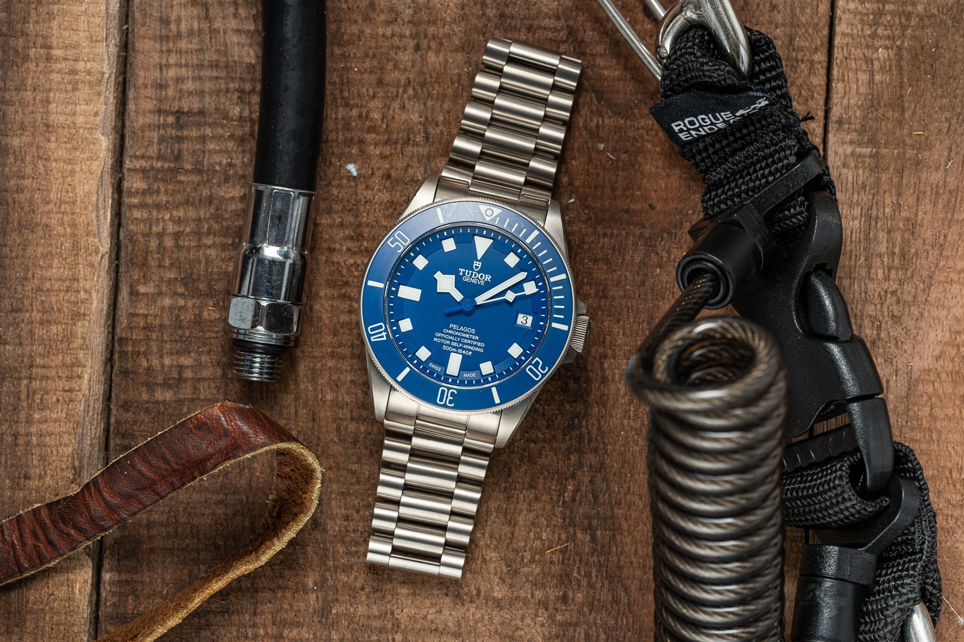 Stainless steel bracelet with polished links and secure clasp displayed on wooden surface next to tactical gear