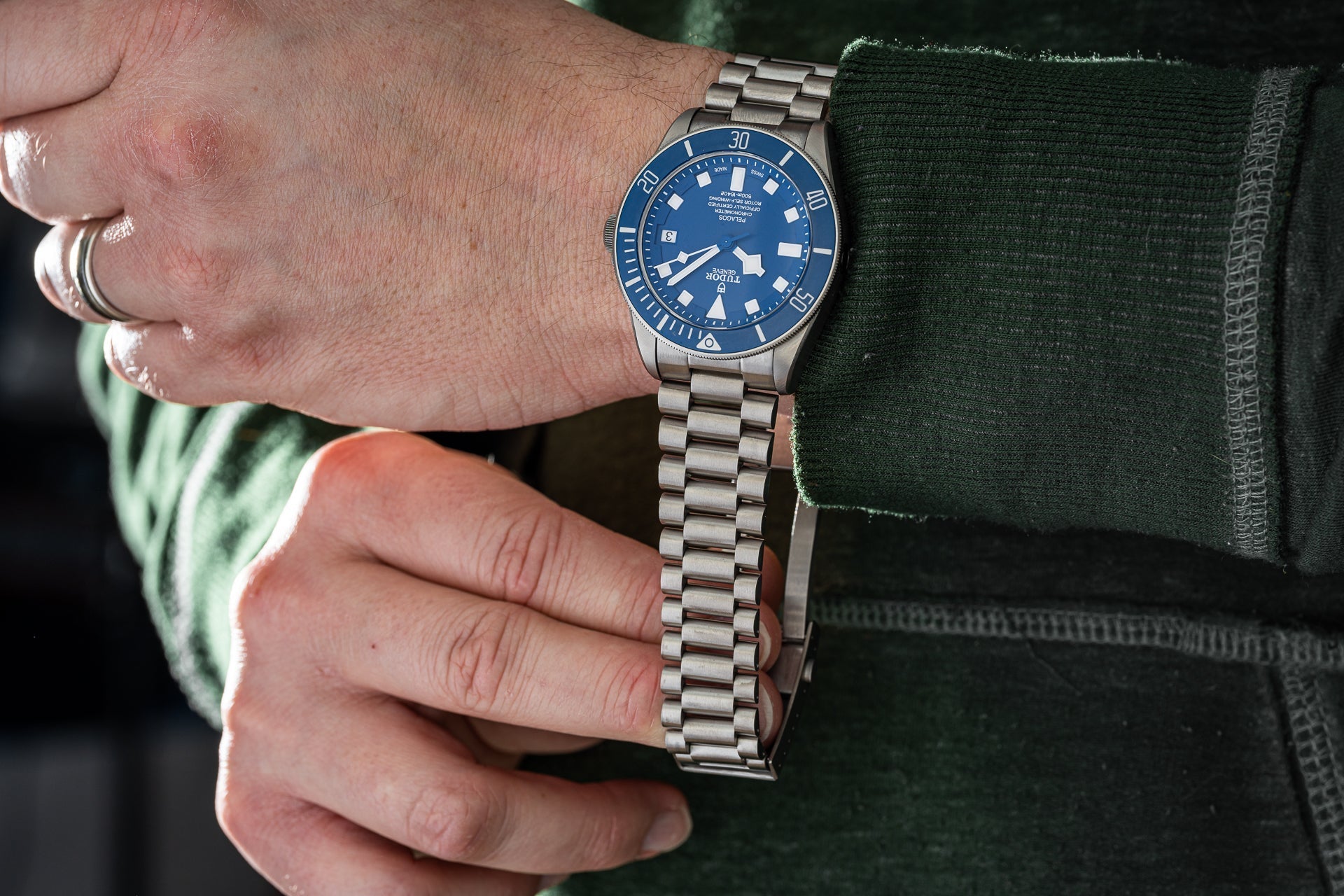 Titanium bracelet with solid link construction and secure clasp system displayed on wrist alongside blue dial dive watch