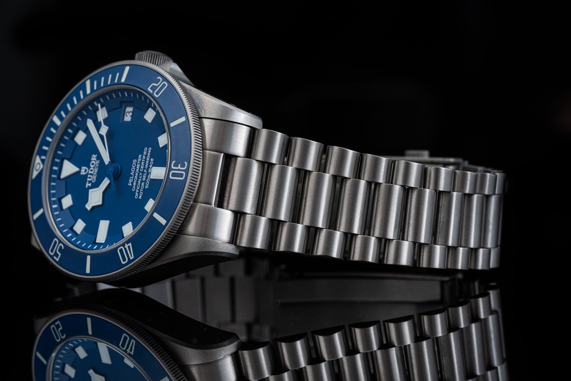 Titanium dive watch with blue dial and unidirectional bezel on stainless steel bracelet against black background