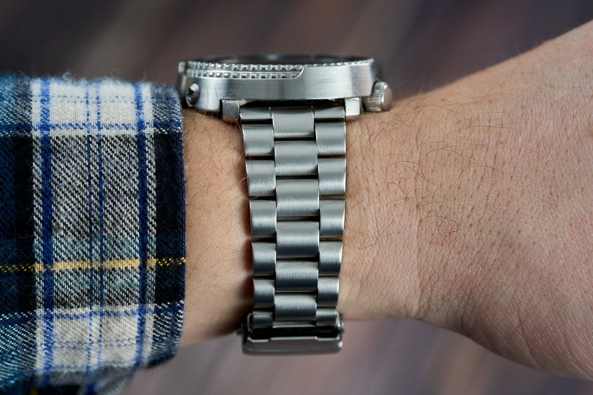 Stainless steel watch bracelet with straight end links worn on wrist with plaid shirt cuff