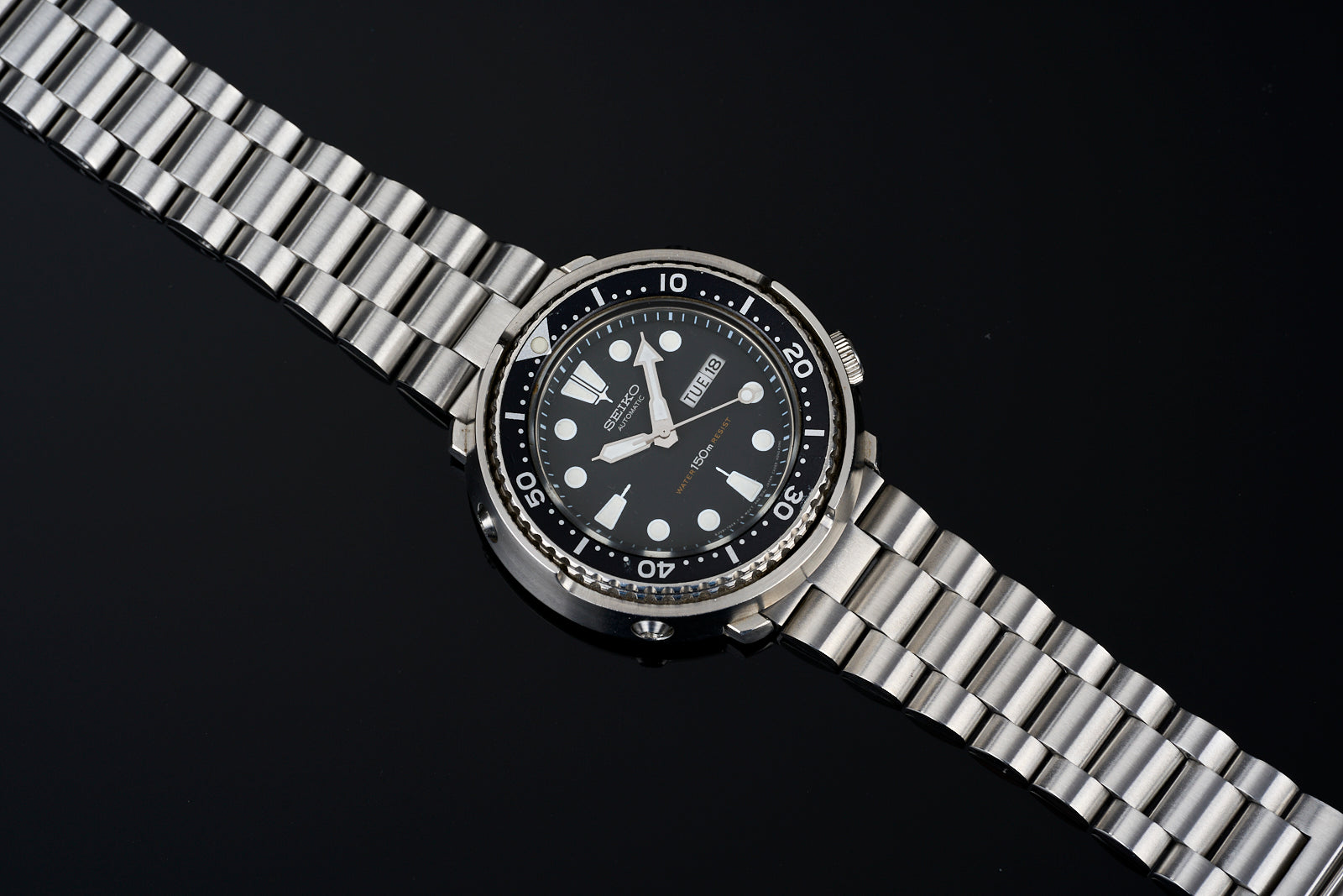Stainless steel diving watch with black dial, white hour markers, and matching metal bracelet on dark background