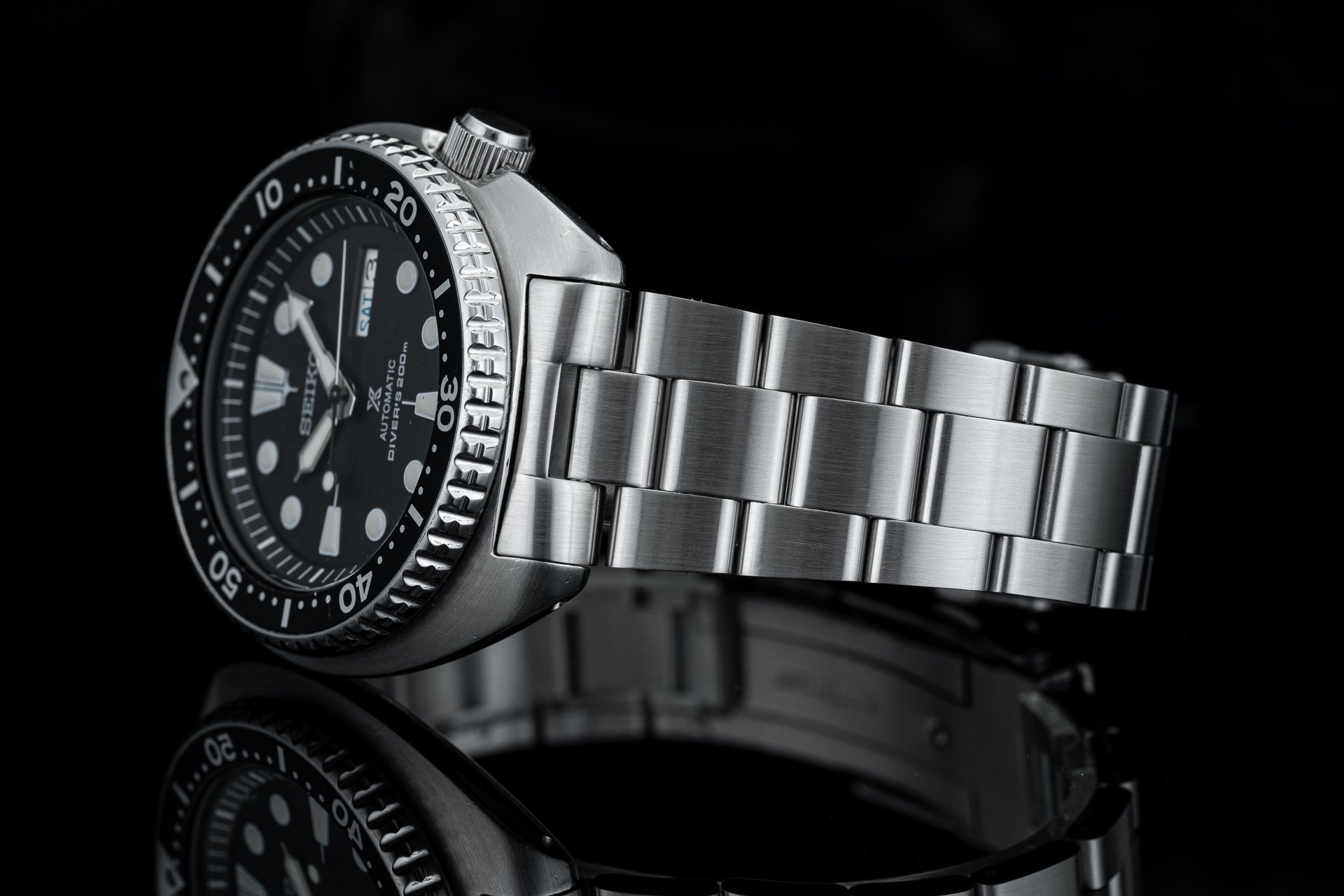 Seiko diver watch with black dial and steel bracelet on black background