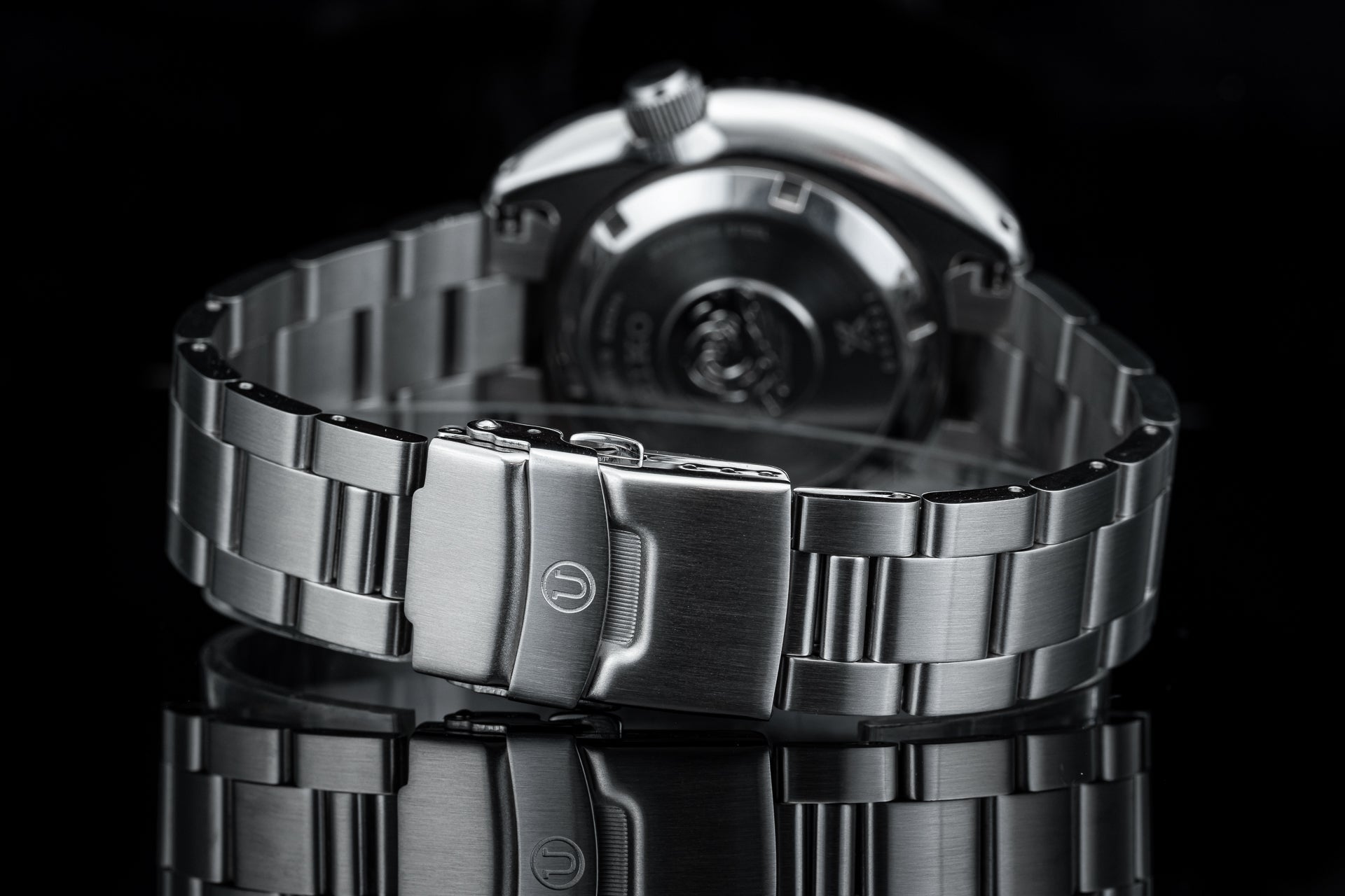Stainless steel dive watch with matching bracelet and fold-over clasp, featuring black dial and rotating bezel on reflective surface