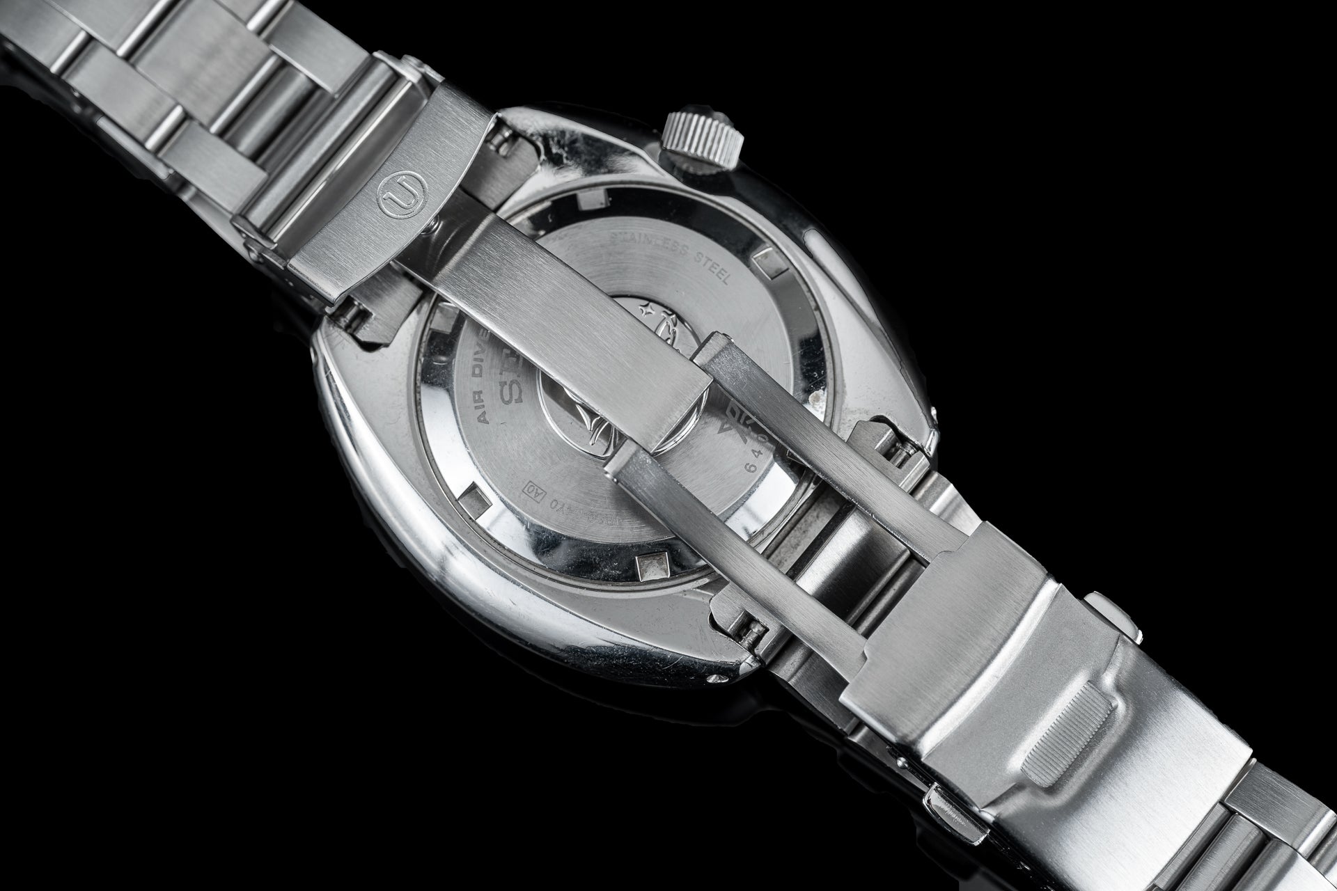 Stainless steel dive watch with Uncle Seiko bracelet and integrated metal links on black background, overhead view