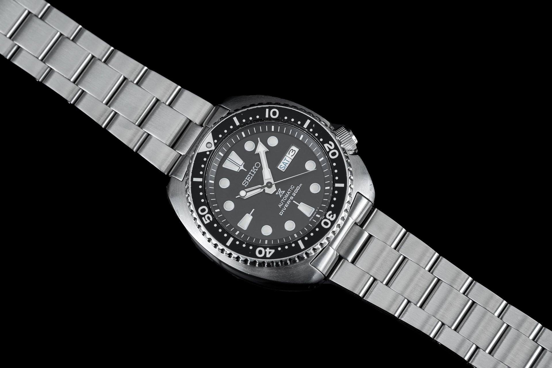 Seiko diving watch with black dial, stainless steel bracelet, date window, and rotating bezel on black background