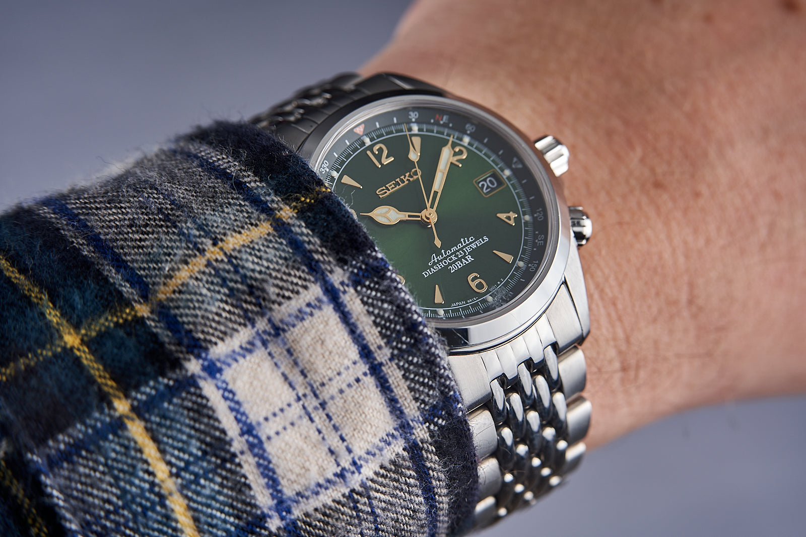 Seiko SARB017 automatic watch with green dial and gold indices on stainless steel bracelet, worn on wrist with plaid fabric