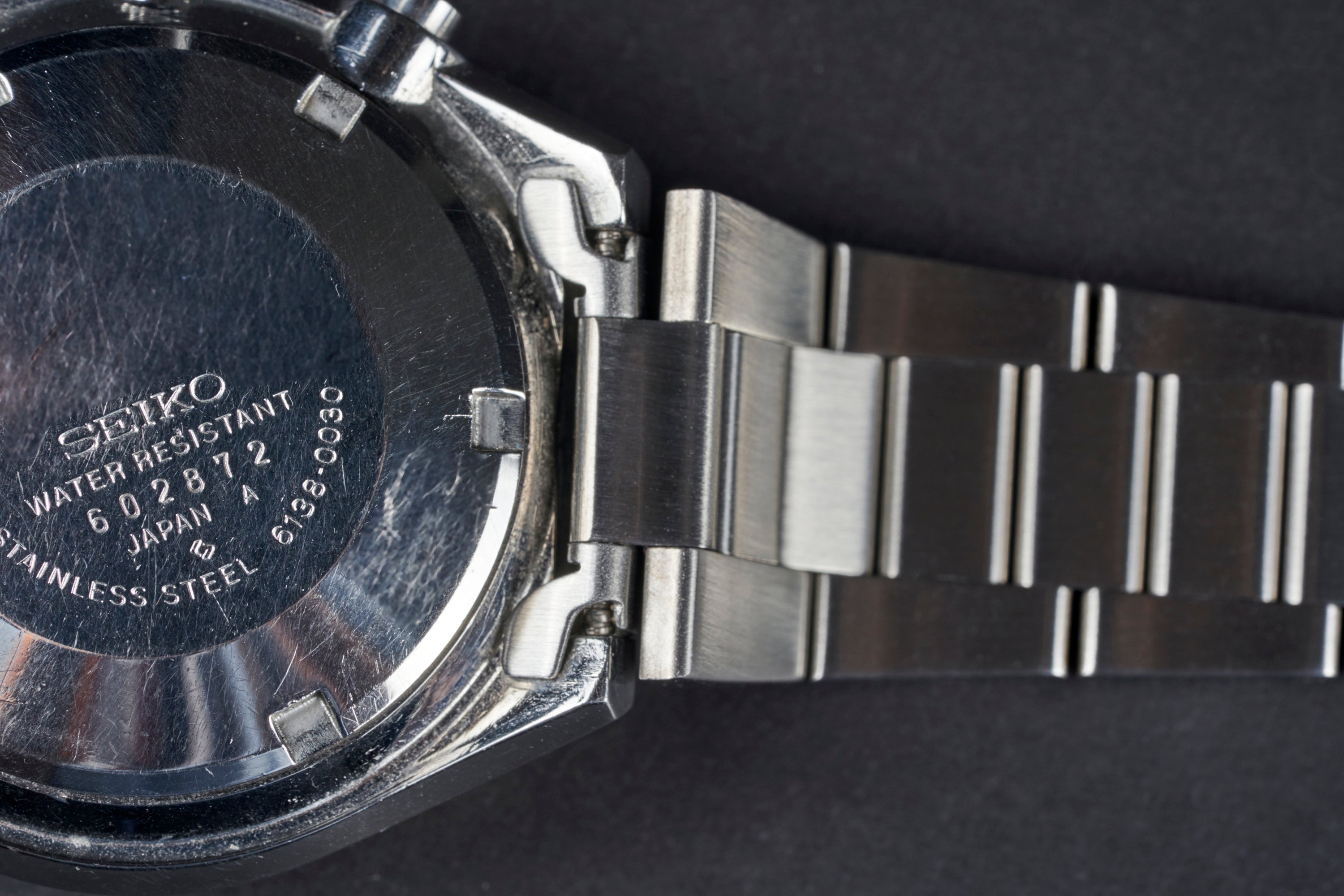 Seiko 6138 watch with water-resistant dark dial, stainless steel tapered bracelet, and Japanese craftsmanship on black background