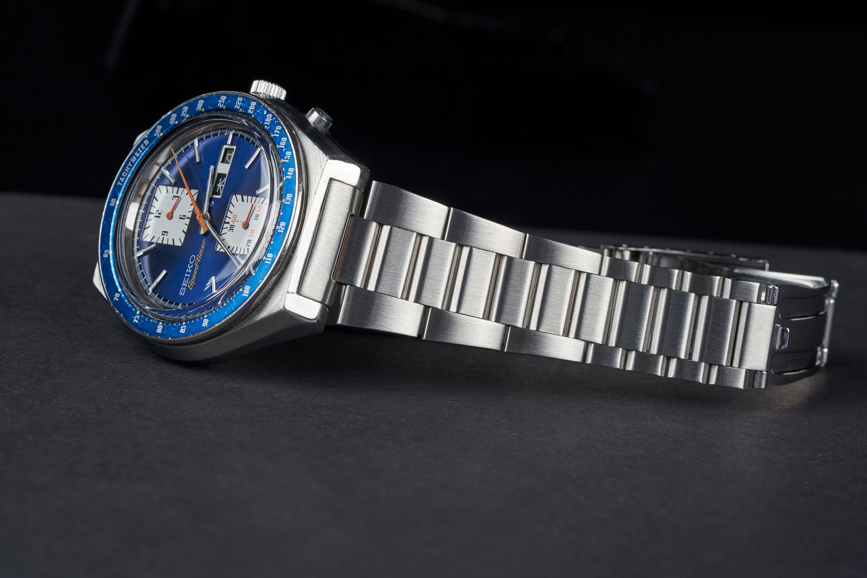 Seiko 6138 chronograph watch with blue dial, white subdials, blue bezel, and stainless steel tapered bracelet on dark background