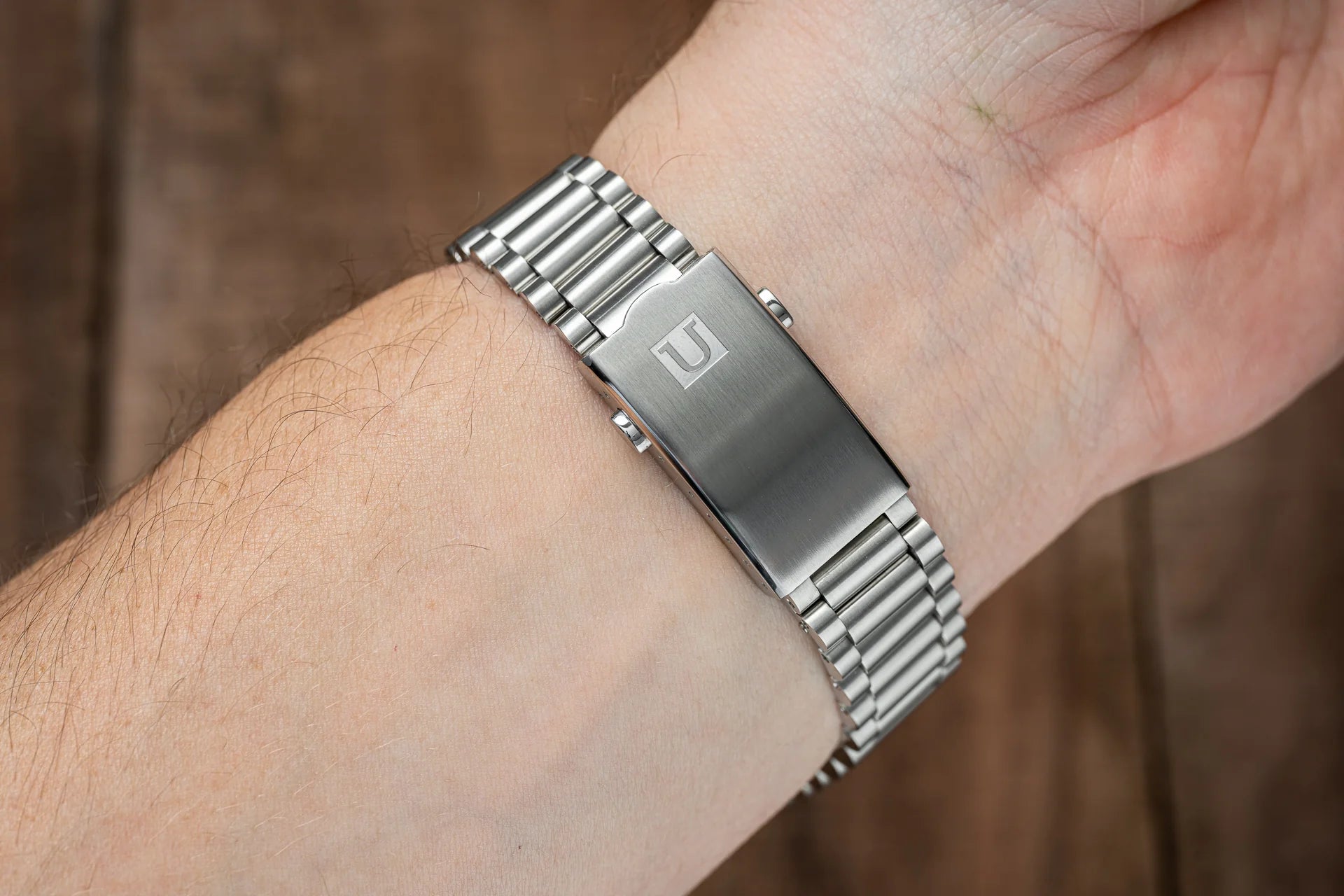 Stainless steel bracelet with polished and brushed finish links on man's wrist, featuring engraved clasp logo