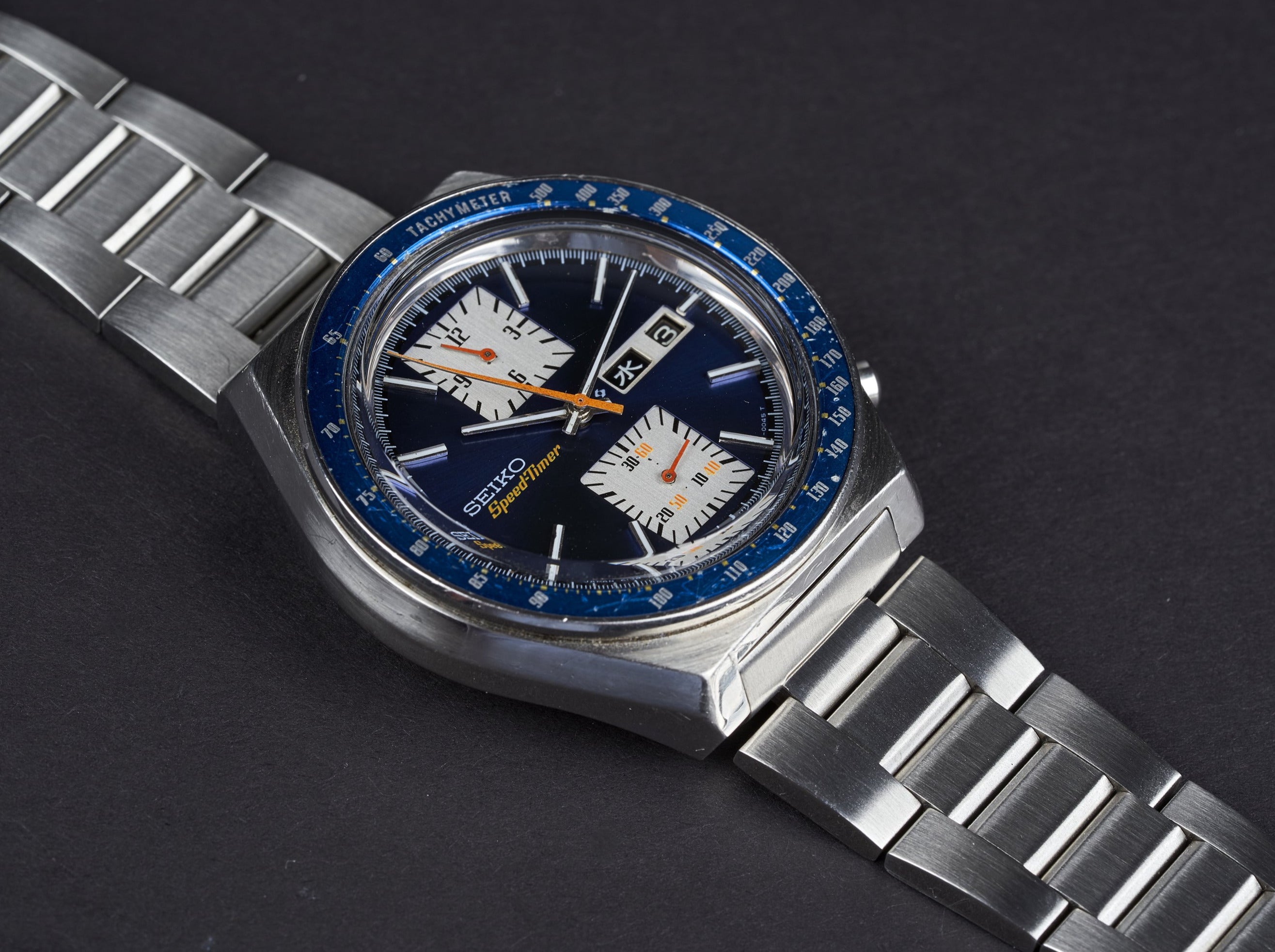 Vintage Seiko 6139 chronograph watch with blue bezel, dark dial, subdials, orange hands and stainless steel bracelet