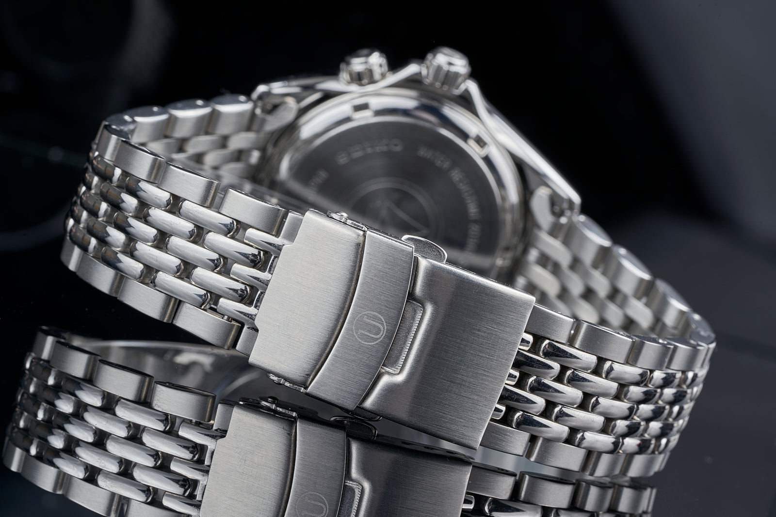 Stainless steel automatic watch with beads of rice bracelet, chronograph pushers, and metallic dial on dark background