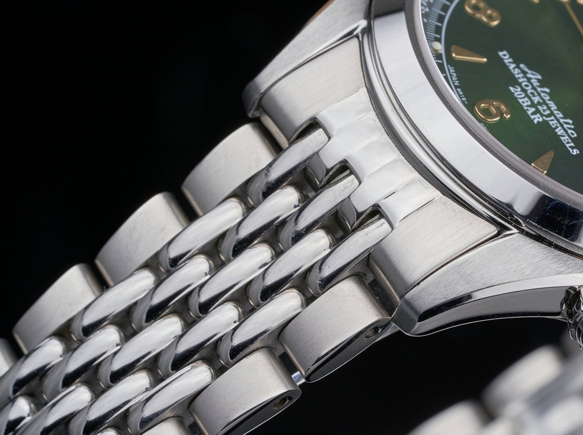 Stainless steel Seiko watch with green dial and beads of rice metal bracelet detail on black background