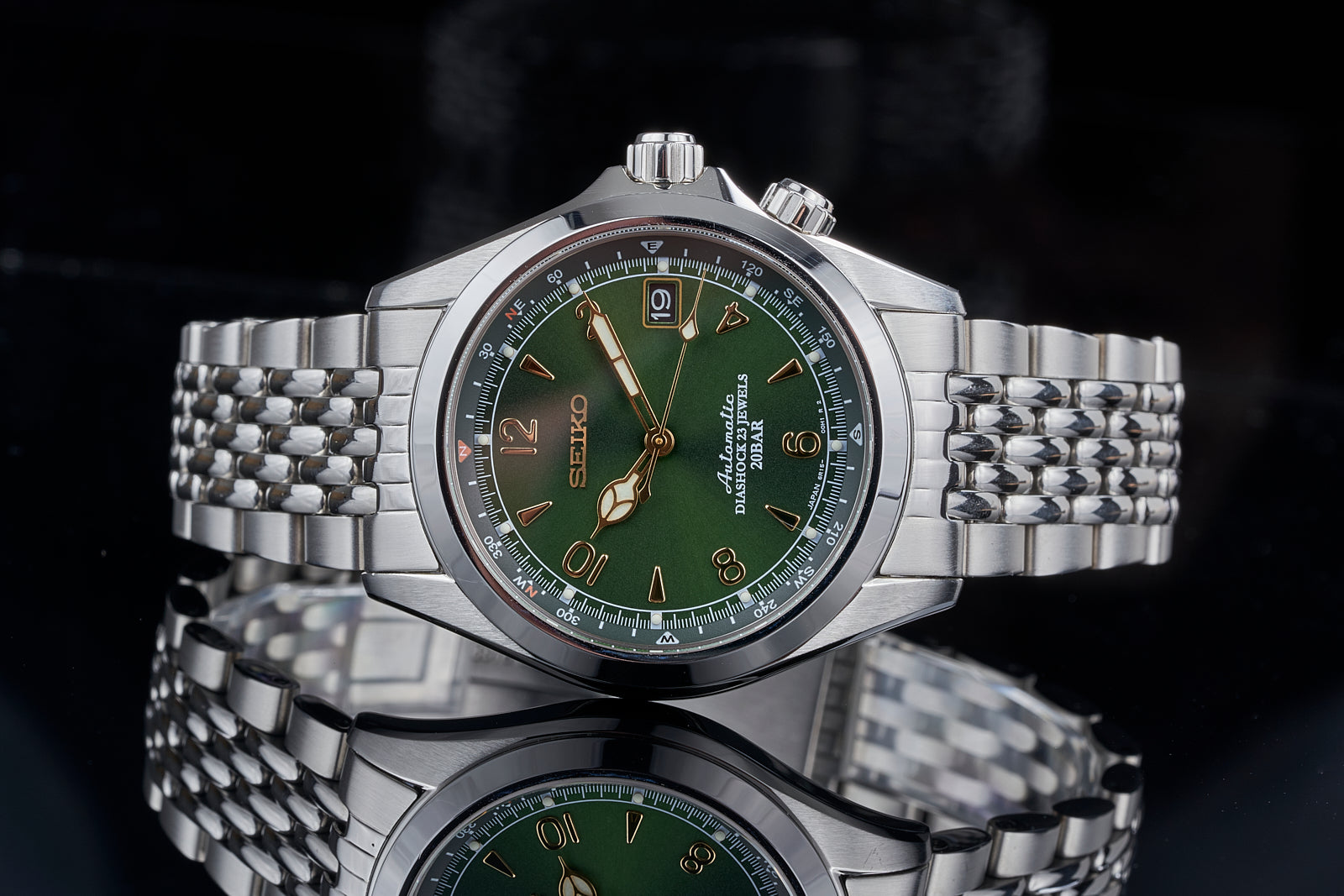 Seiko Alpinist stainless steel watch with green dial, gold Arabic numerals, and matching beads of rice bracelet on black background