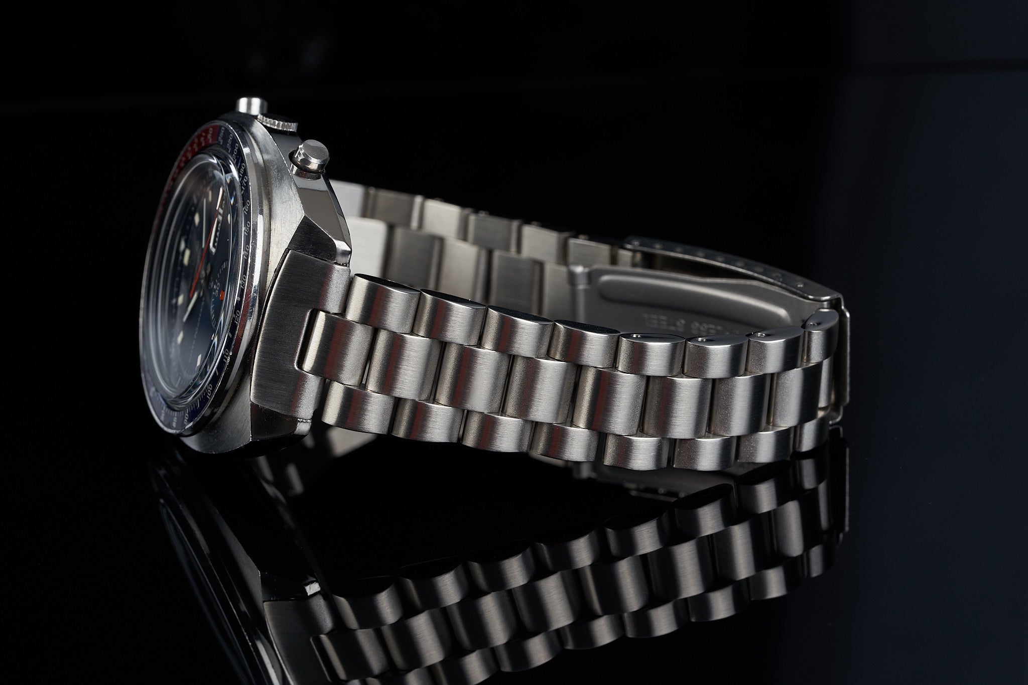 Stainless steel chronograph watch with blue and red dial, featuring linked metal bracelet on black background