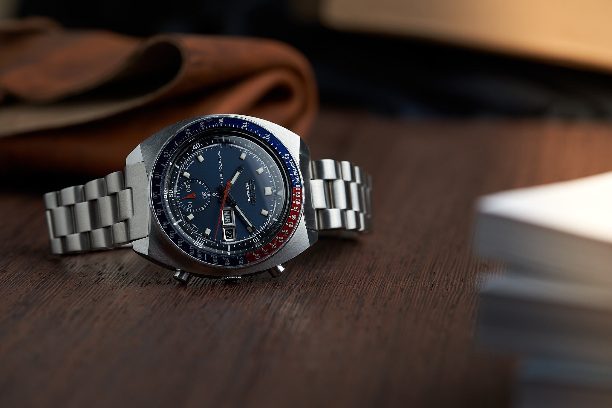 Vintage Seiko 6139 chronograph watch with steel bracelet, blue dial, red and blue bezel on wooden surface