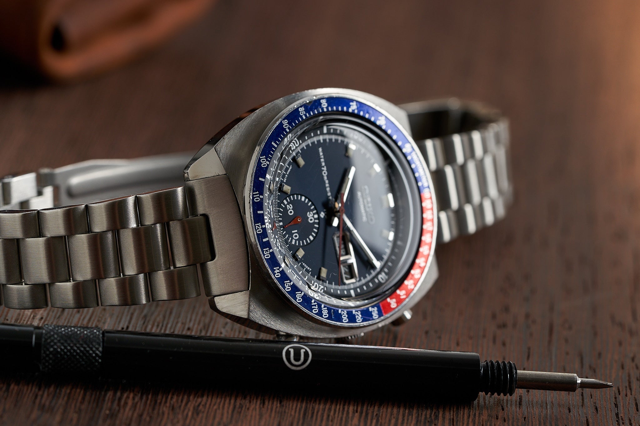 Vintage Seiko 6139-6002 chronograph watch with steel bracelet, blue and red bezel, black dial on wooden surface