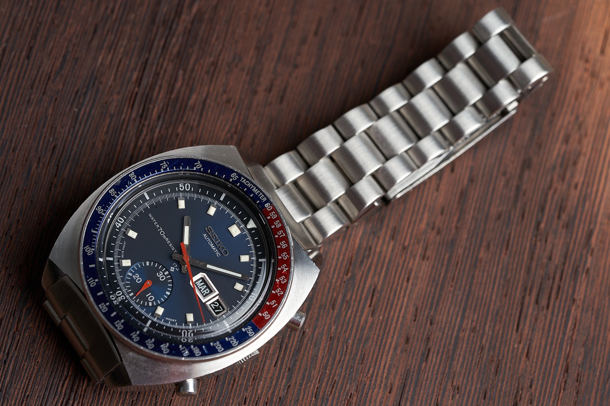 Vintage Seiko 6139-6002 chronograph watch with steel bracelet, blue and red bezel on wooden surface