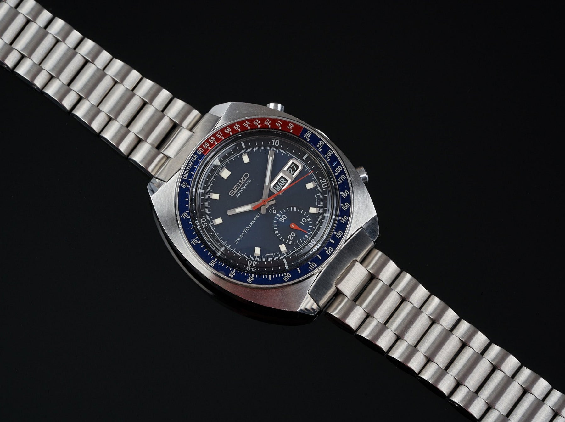 Vintage Seiko chronograph watch with stainless steel bracelet, black dial, red and blue bezel on black background