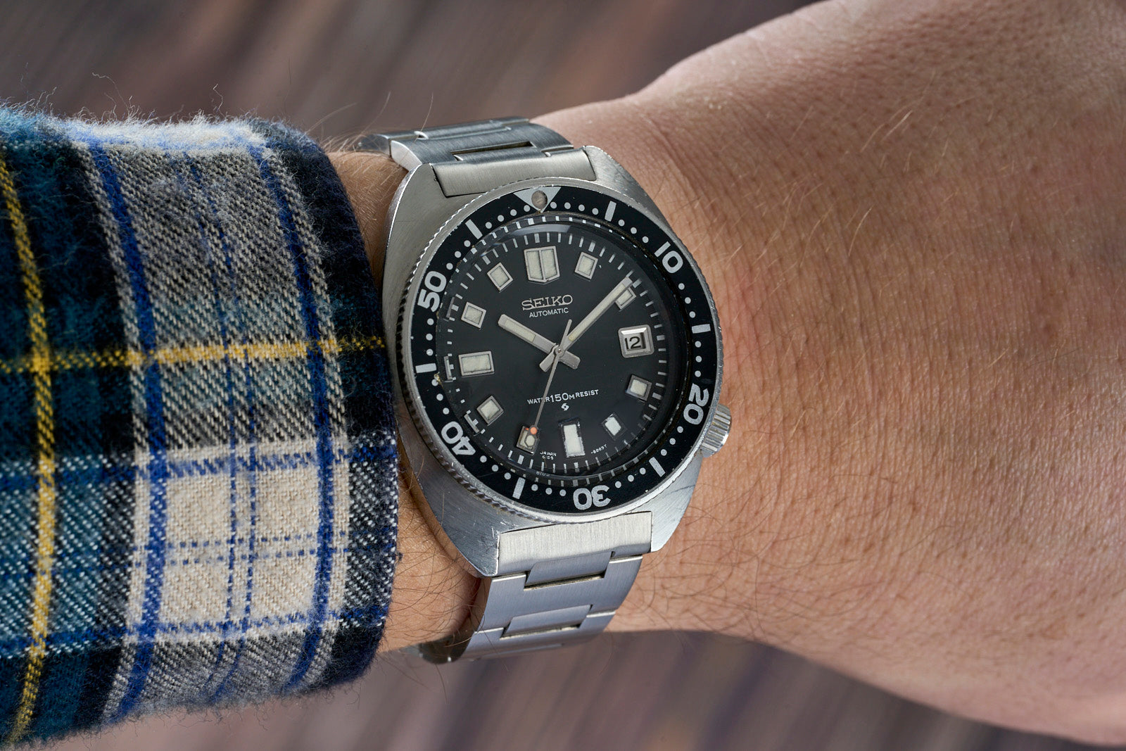 Seiko automatic diving watch with black dial, stainless steel bracelet and bezel on wrist with plaid fabric cuff