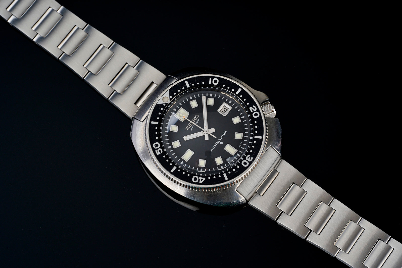 Vintage Seiko 6105 dive watch with black dial, square hour markers, date window, stainless steel H-link bracelet on black background