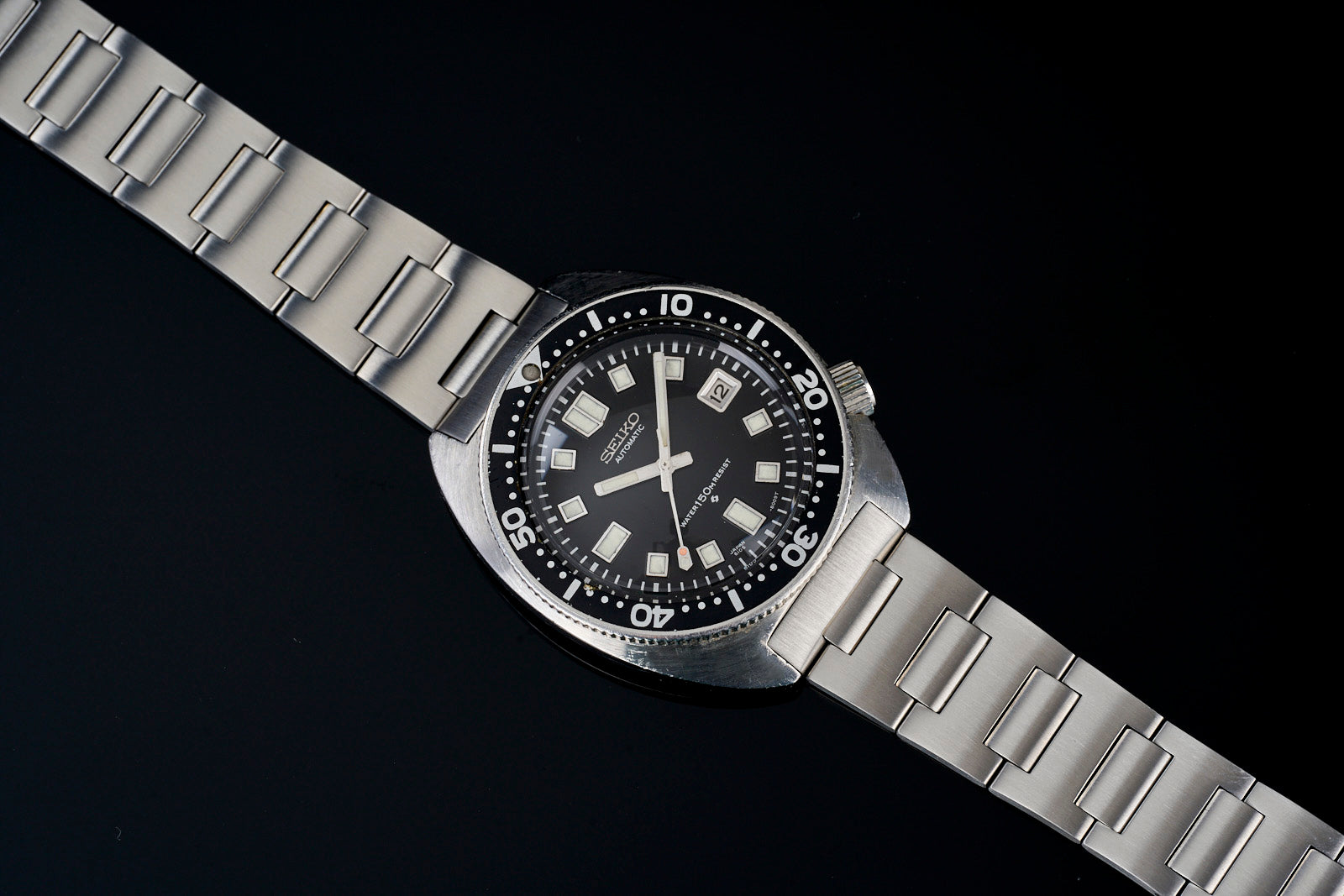 Seiko 6105 dive watch with black dial, stainless steel H-link bracelet, date window, and rotating bezel on black background