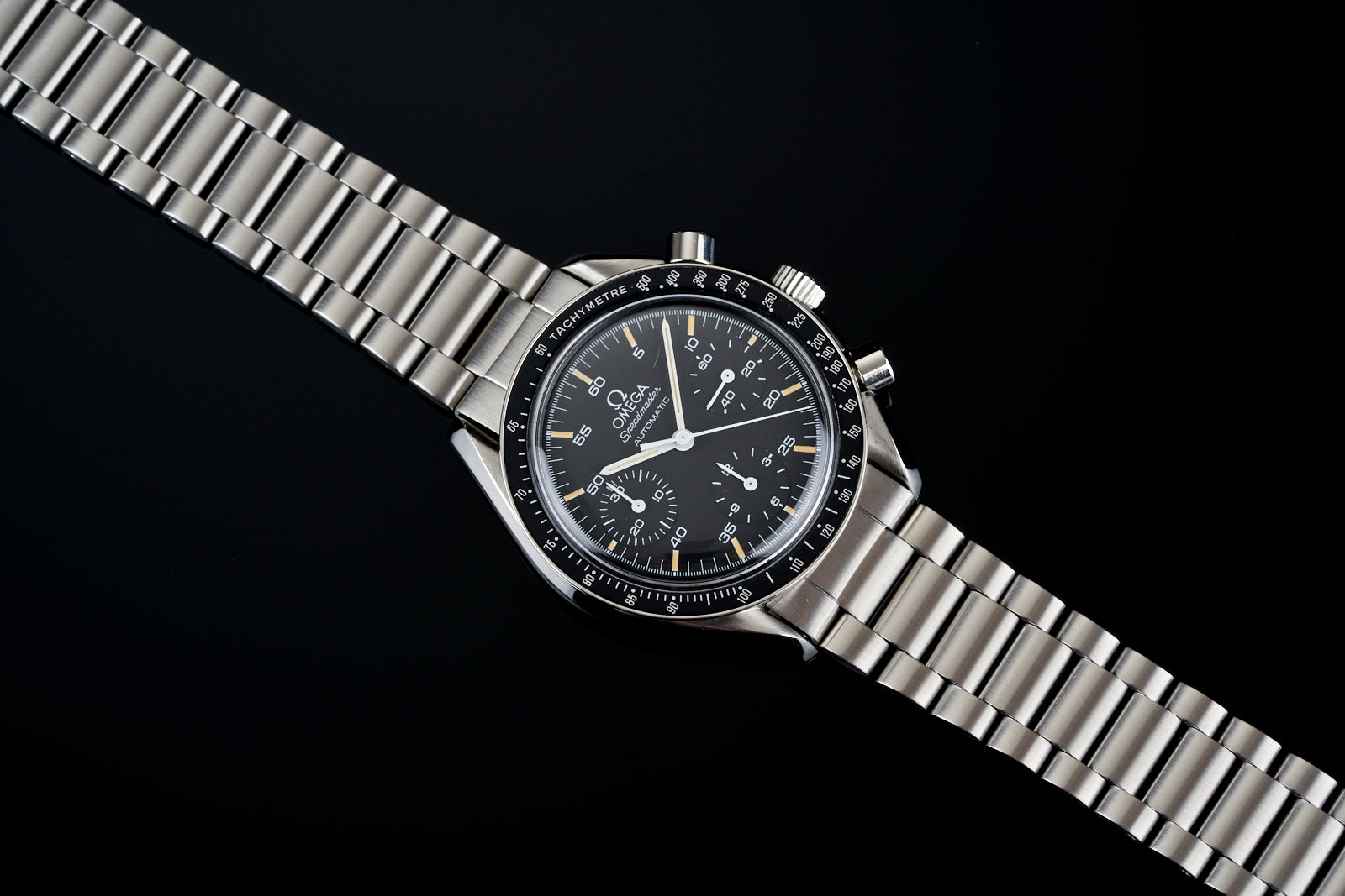 Omega Speedmaster Reduced chronograph watch with stainless steel bracelet and black dial on black background