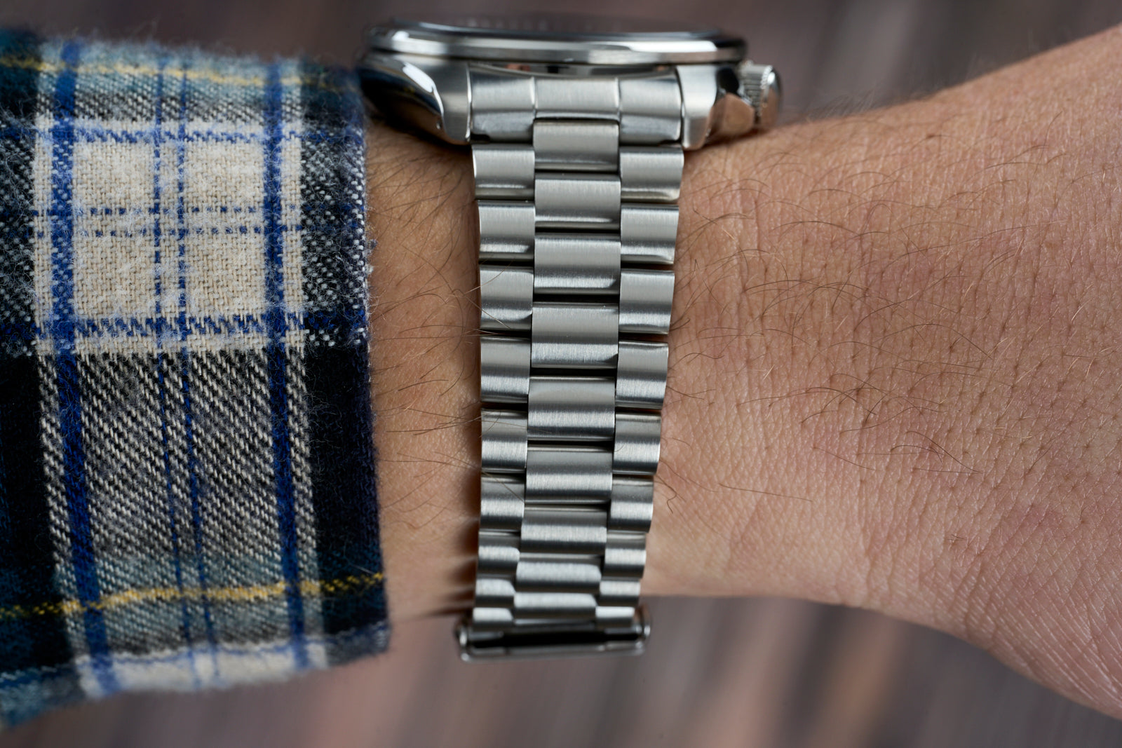 Stainless steel watch bracelet worn on wrist with plaid shirt cuff, showing polished metal links and brushed finish details