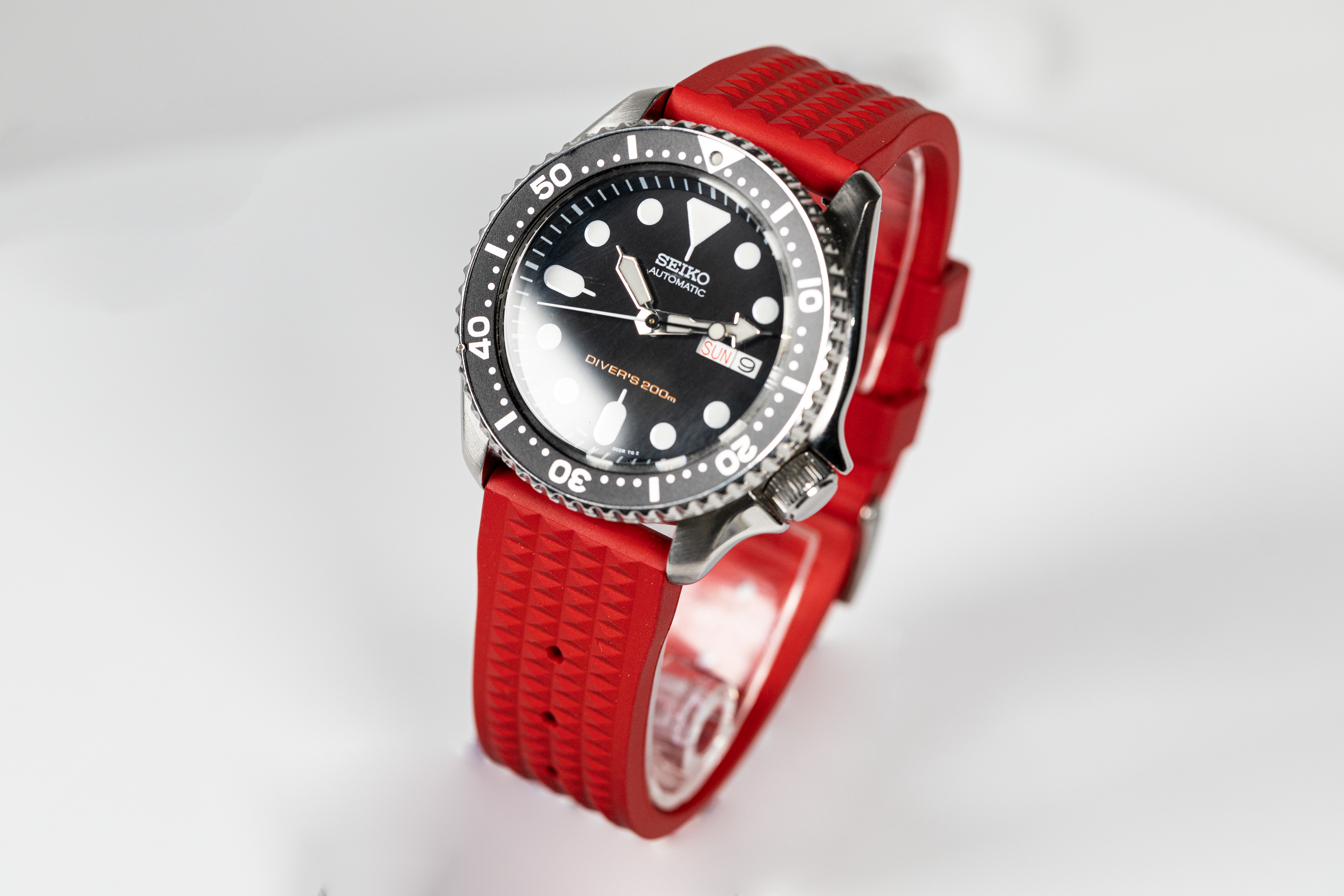 Seiko automatic dive watch with black dial, rotating bezel, and red rubber strap with waffle pattern texture
